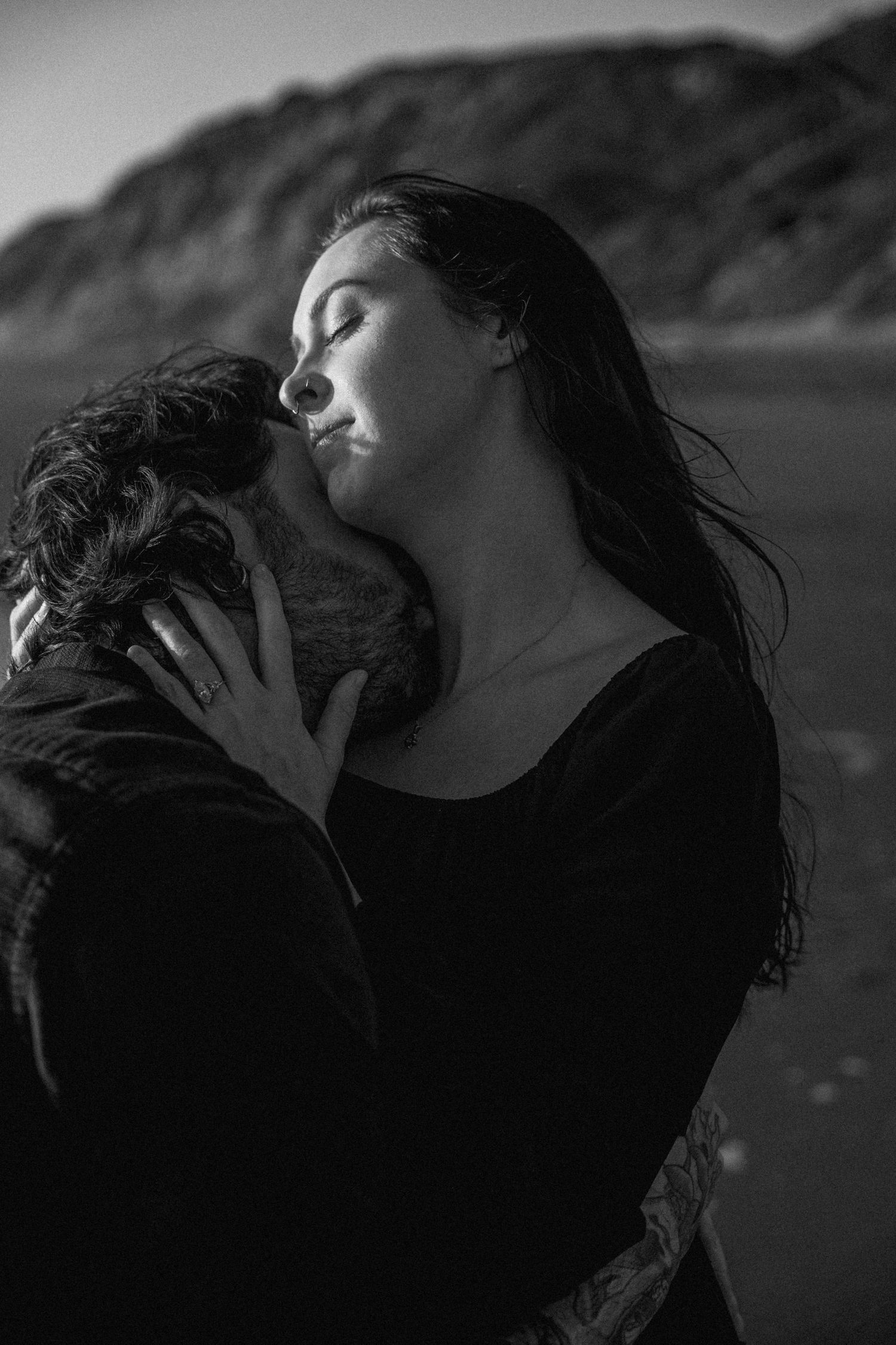 Romantic black and white photo of a couple embracing and kissing on a rocky beach.