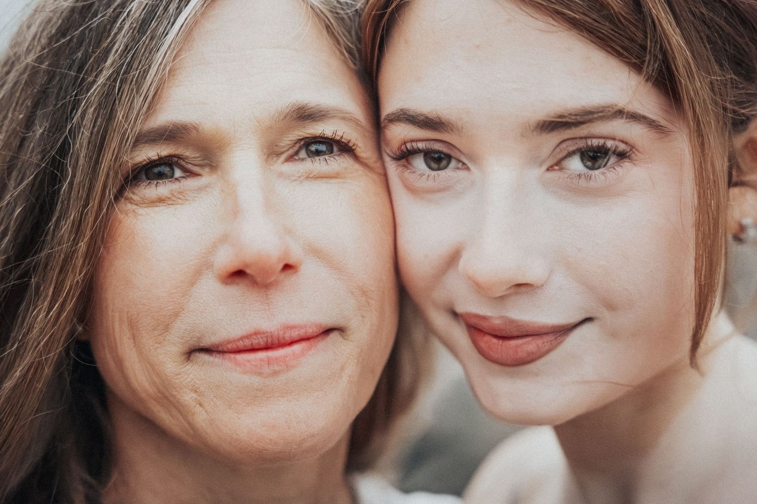 A close-up portrait of two women with brown hair smiling warmly cheek to cheek.