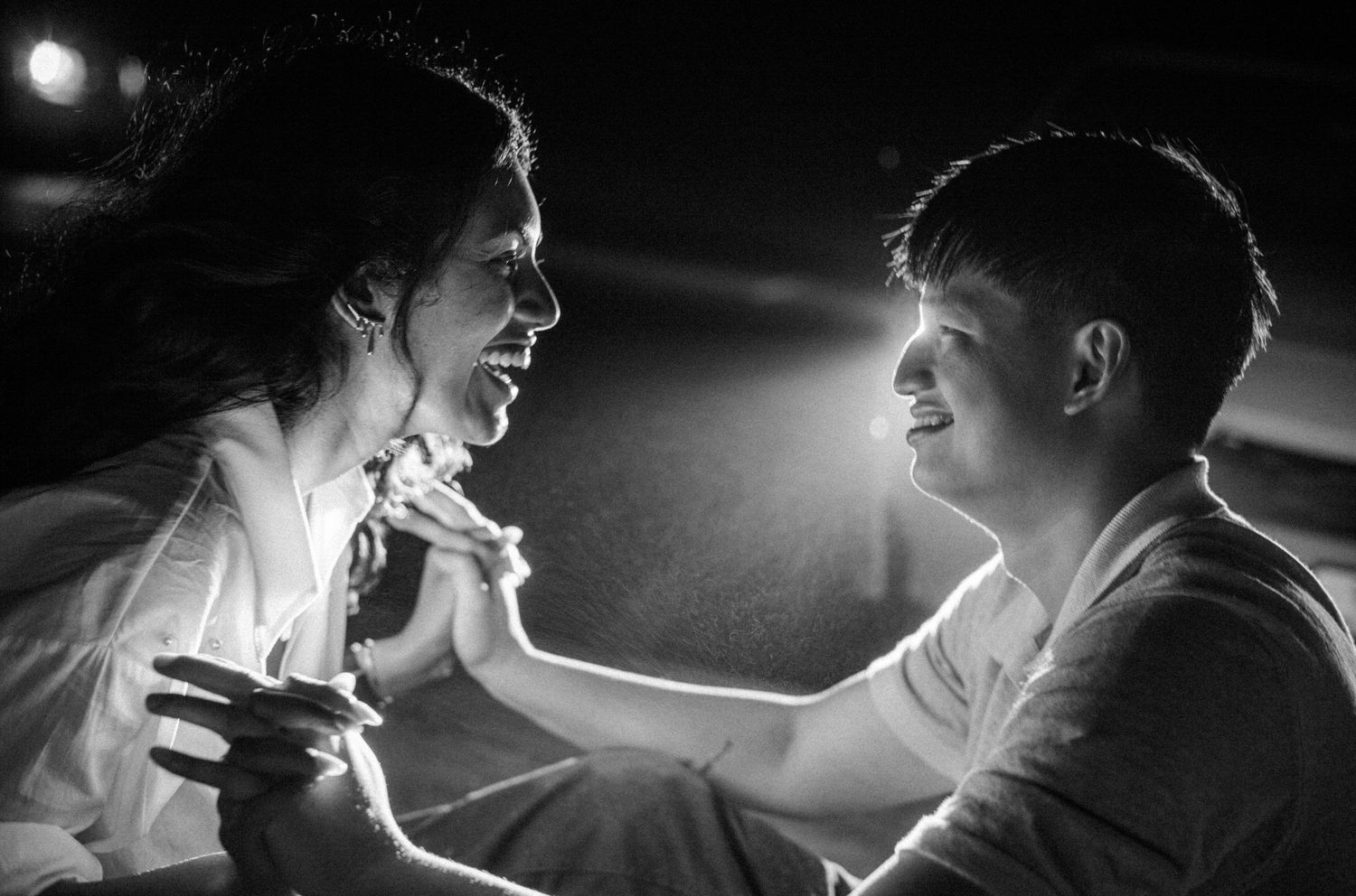 Black and white photo of a joyful couple holding hands and smiling at each other in a romantic moment.