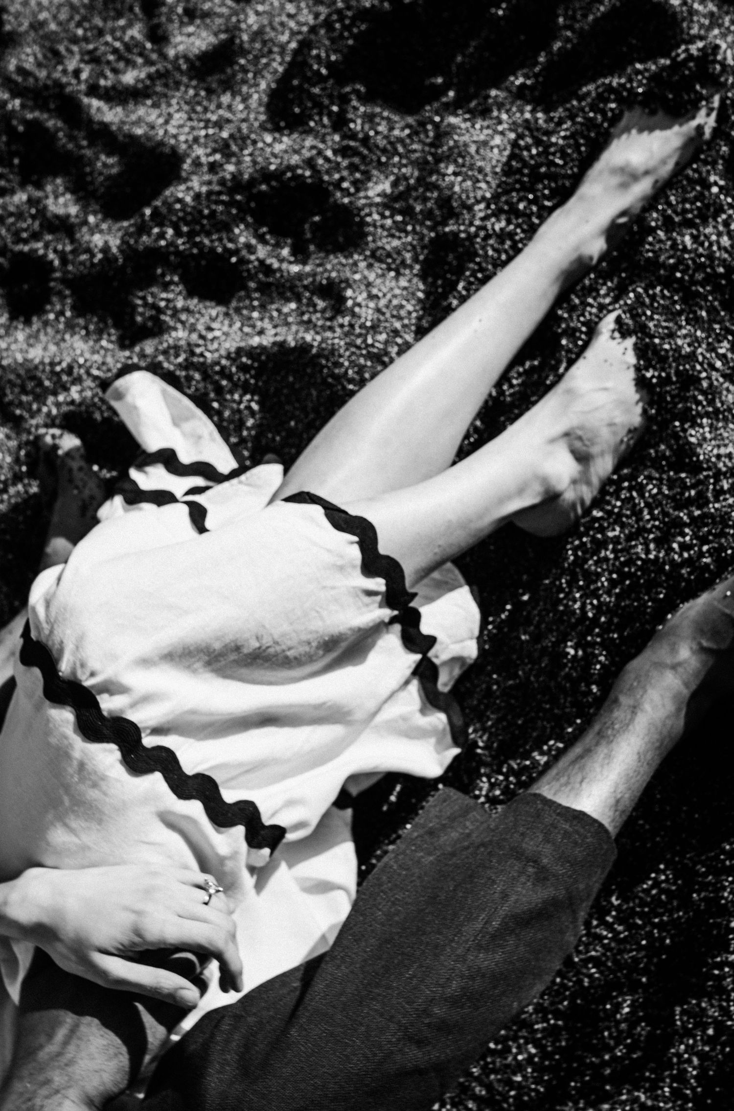 Black and white photo of a couple lying on grass, woman in white dress with black trim, bare legs visible.Photography by The Y.K. Studio.