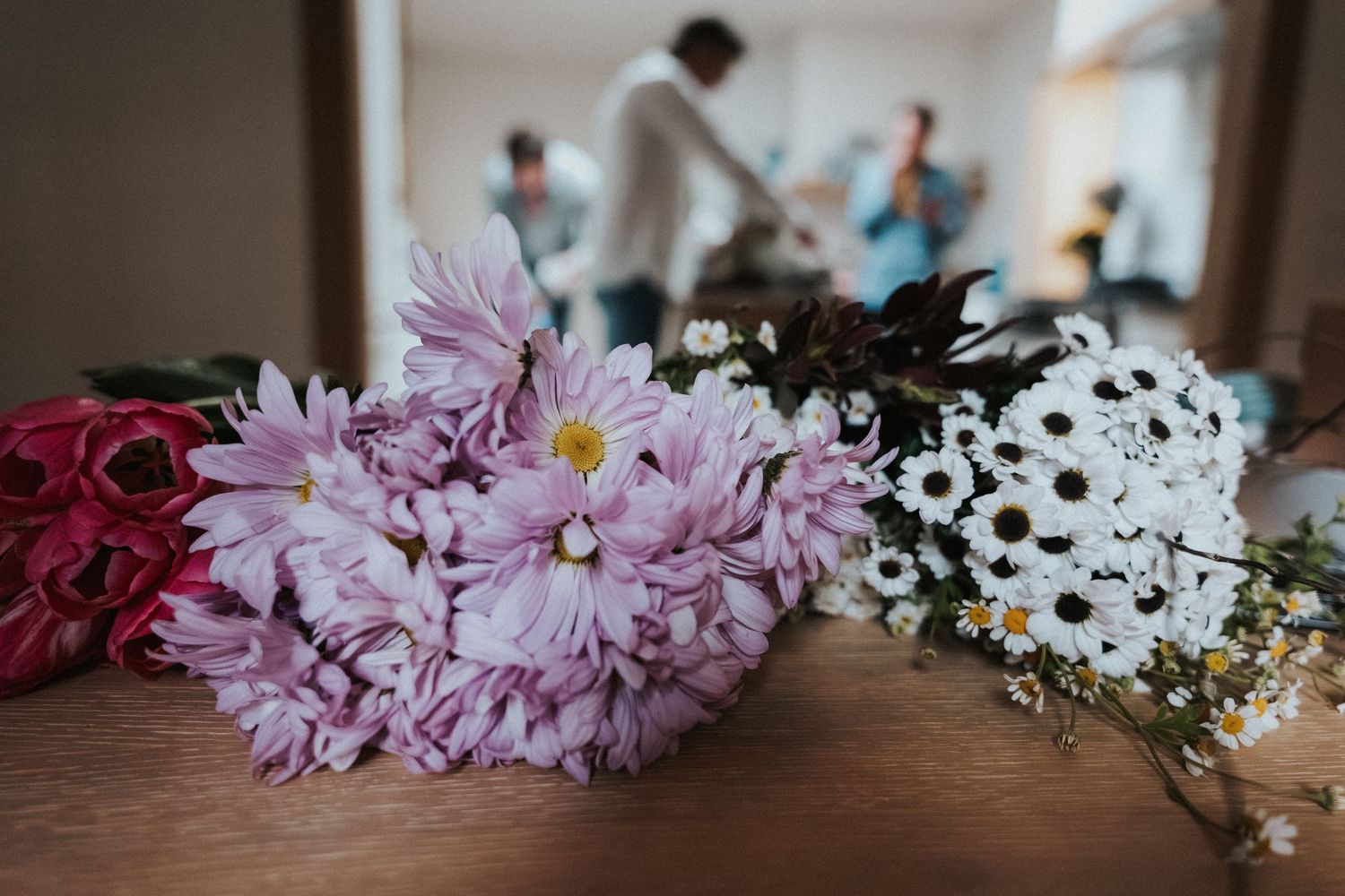 Colorful wedding flowers including pink chrysanthemums and white daisies arranged on a wooden table.