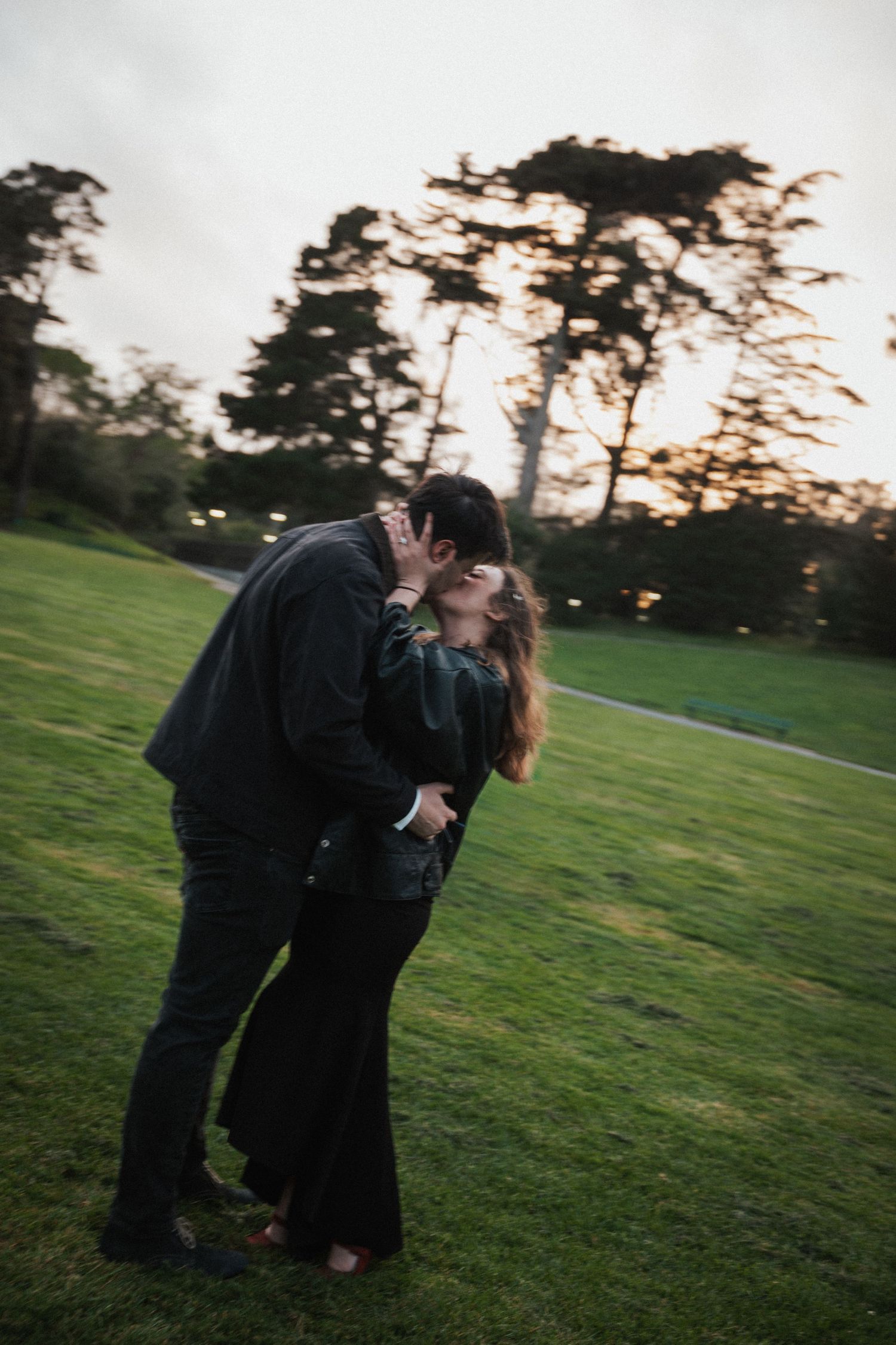 Romantic couple sharing a passionate kiss on a grassy field at sunset.