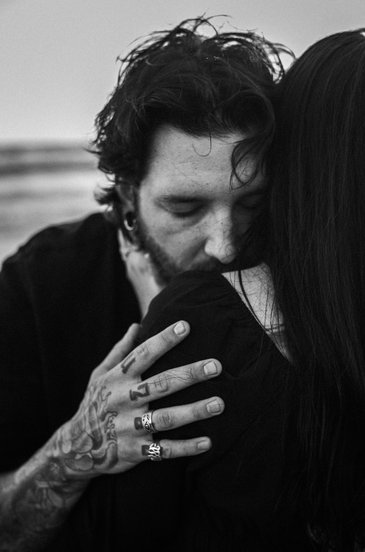 Tattooed man with rings tenderly kissing womans shoulder in intimate black and white close-up.