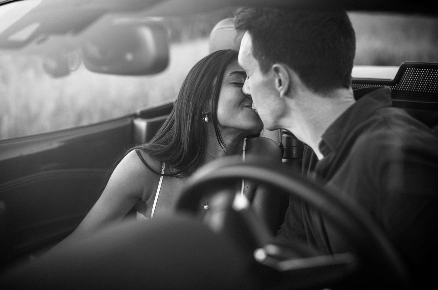Romantic black and white photo of a couple sharing a kiss inside a sports car.