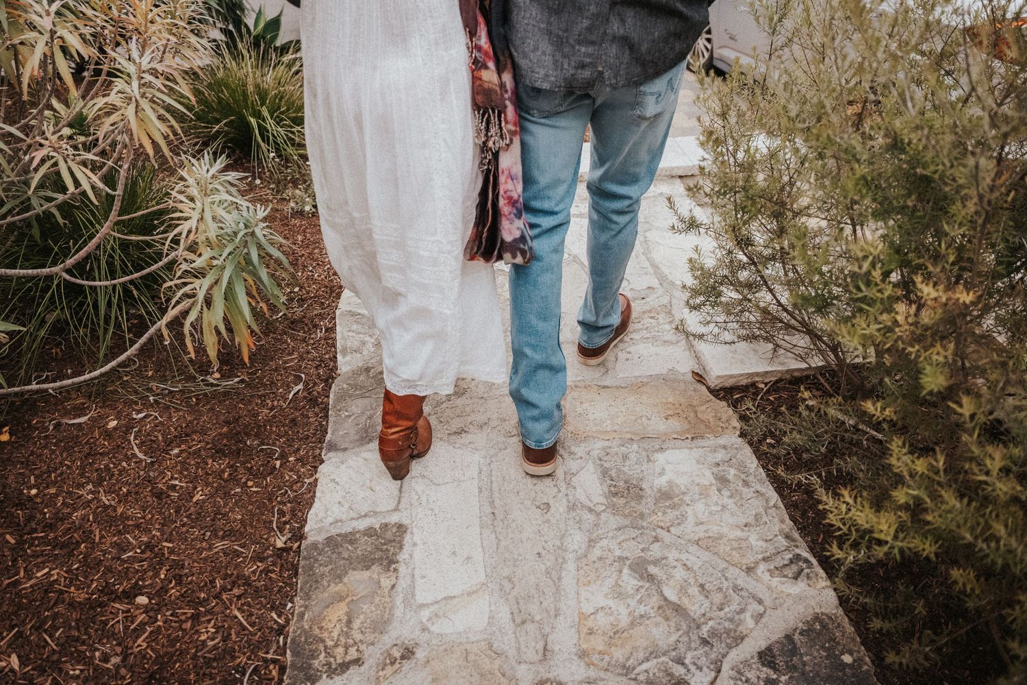 Bride and groom walking hand in hand along a stone garden path on their wedding day.