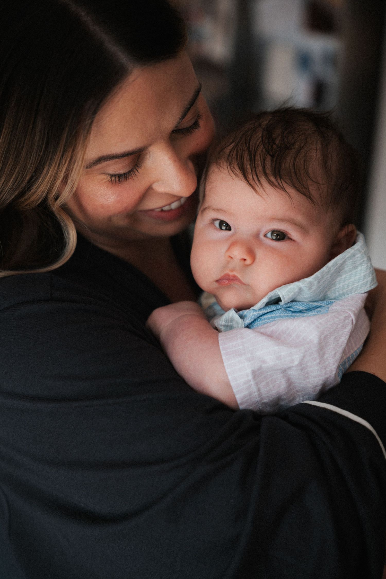 A smiling mother tenderly holds her newborn baby dressed in a light blue outfit, sharing a loving moment.