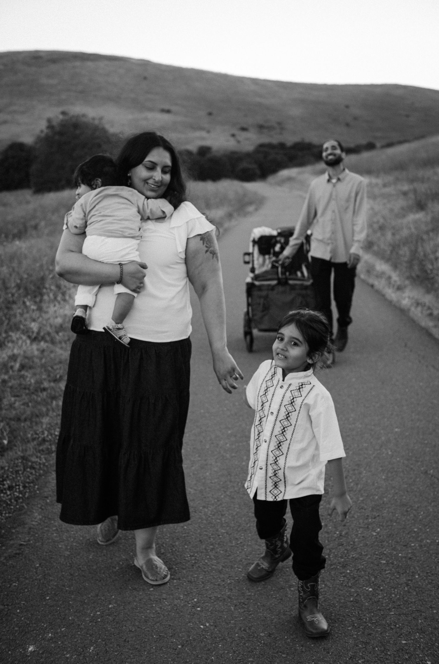 Black and white family portrait on a path with mother holding baby and young son.