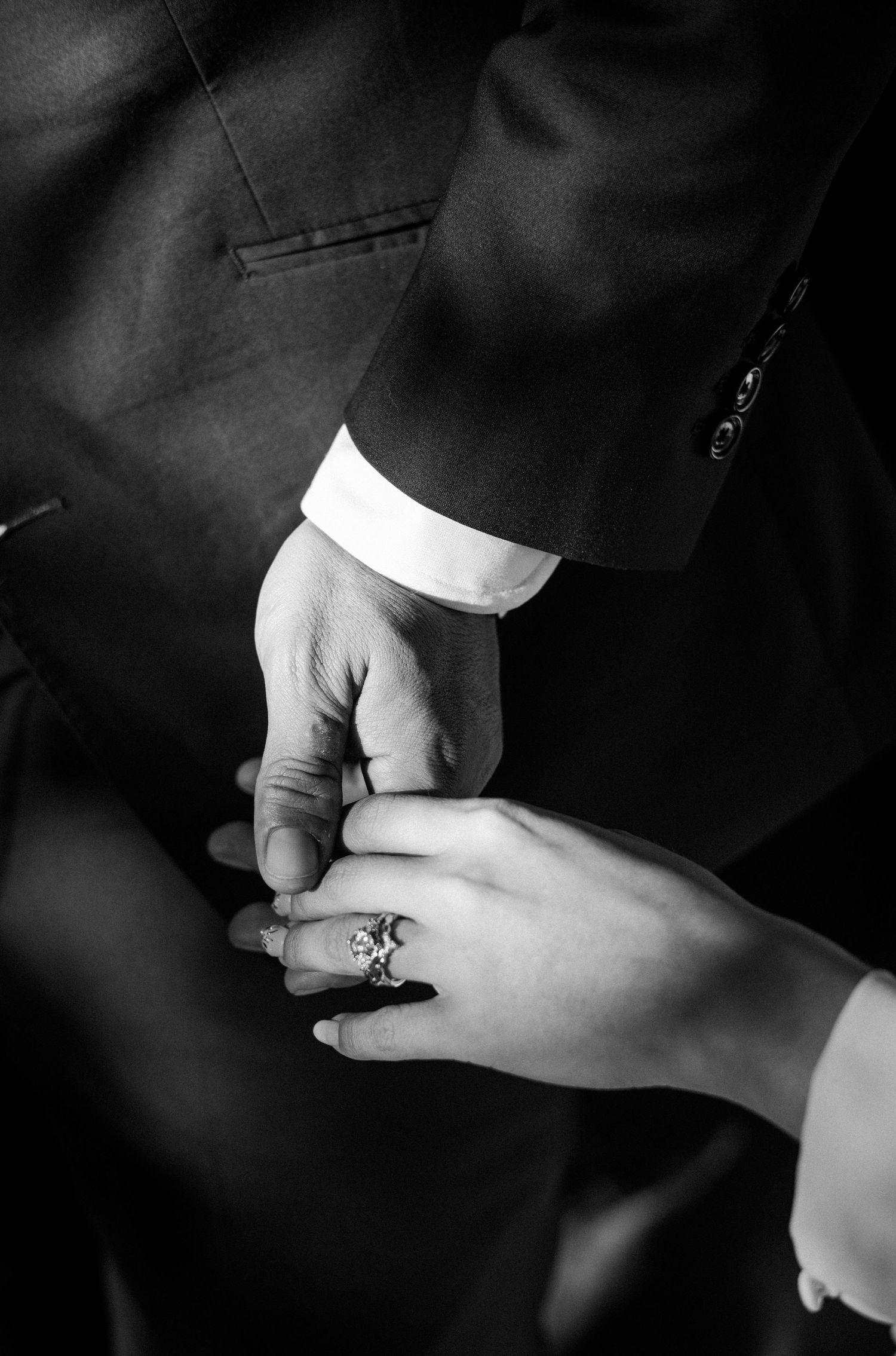 Black and white photo of a couple holding hands, showcasing an elegant diamond engagement ring during a wedding ceremony.