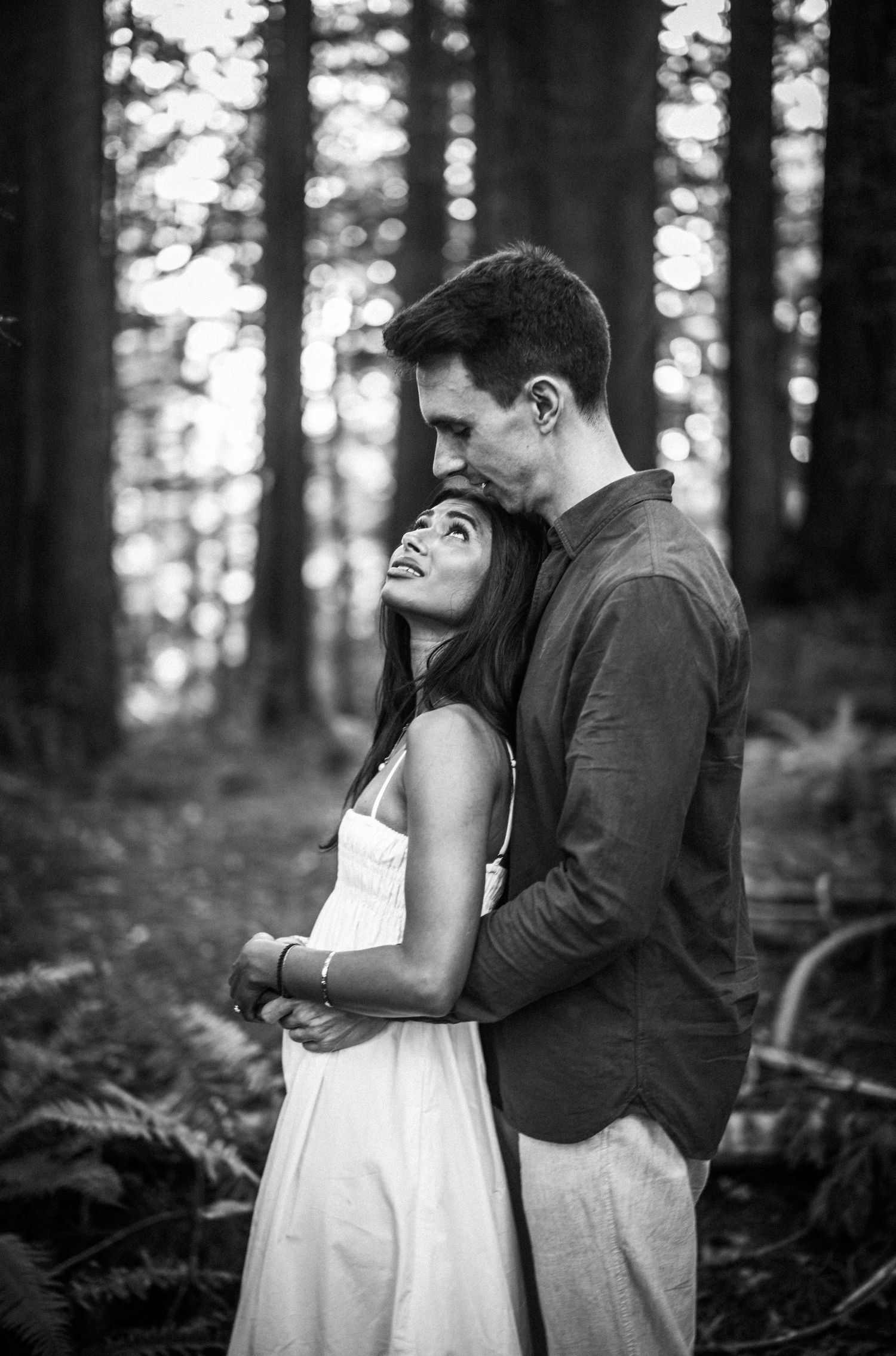 Black and white photo of couple embracing tenderly in a serene forest setting.
