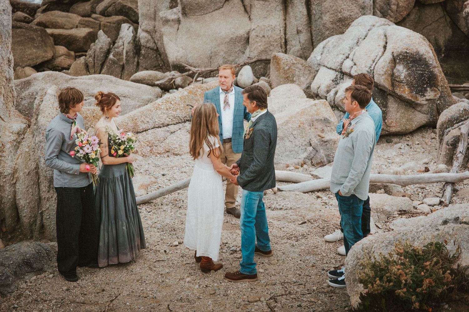 Small outdoor wedding ceremony among rocky boulders with bride, groom, officiant, and wedding party.