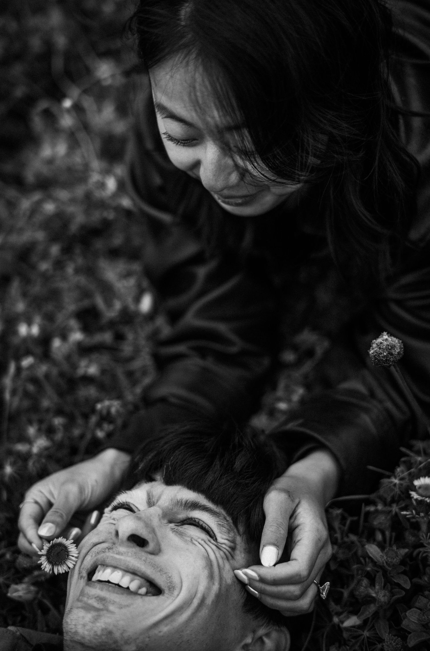 Black and white photo of a smiling man lying on ground while a woman kneels beside him holding a flower.