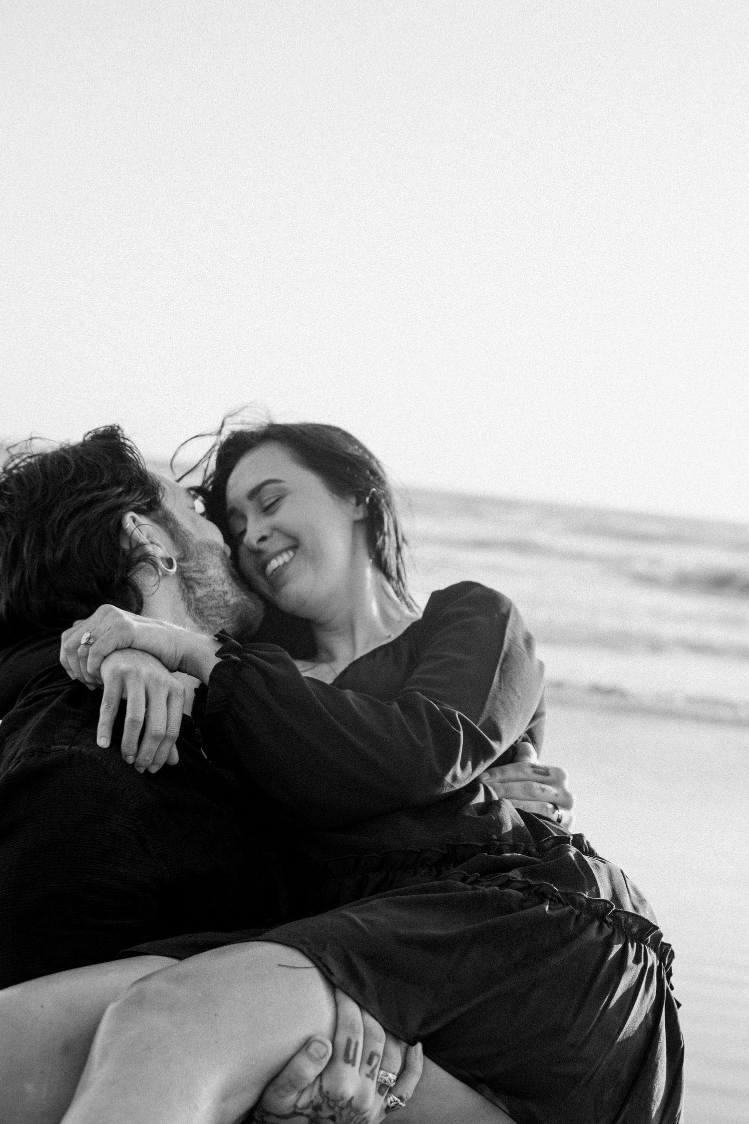 Black and white photo of a joyful couple embracing and laughing together on a beach.