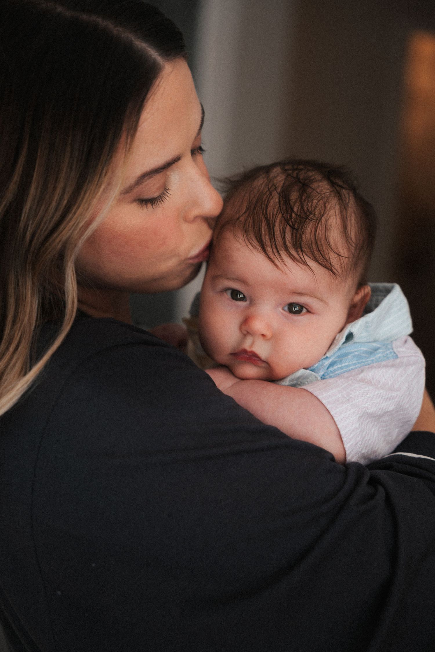 A mother tenderly kisses her newborn baby while cradling the infant in her arms.
