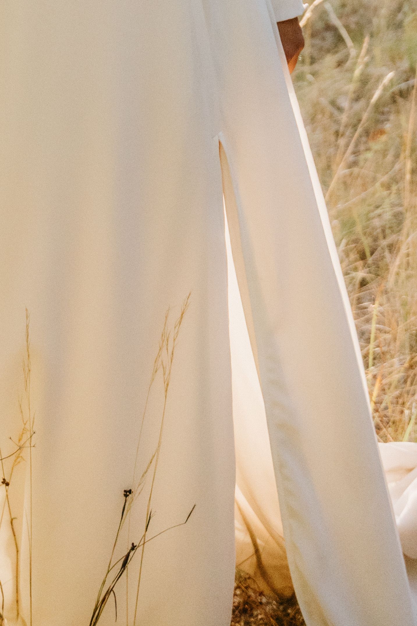 Close-up of a flowing white dress with a side slit, set against a natural dry grass background.