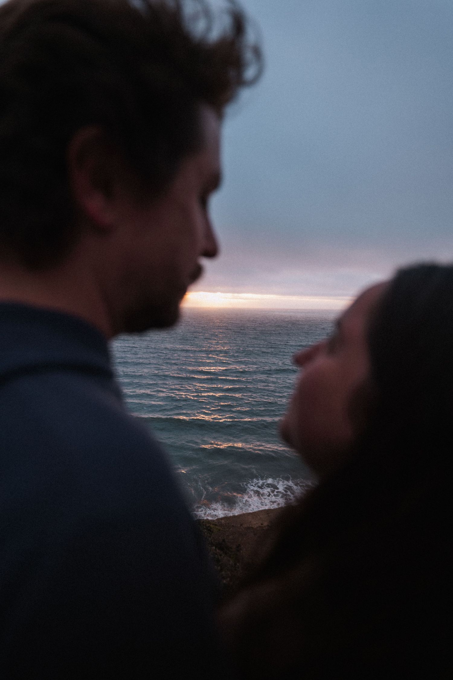 A romantic couple shares an intimate moment at sunset overlooking the ocean waves.