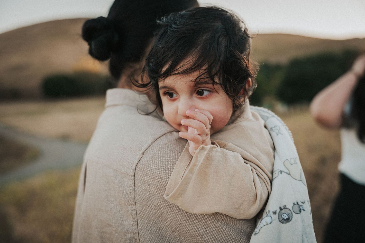 A young child resting their chin on an adult's shoulder during a golden hour outdoor embrace.