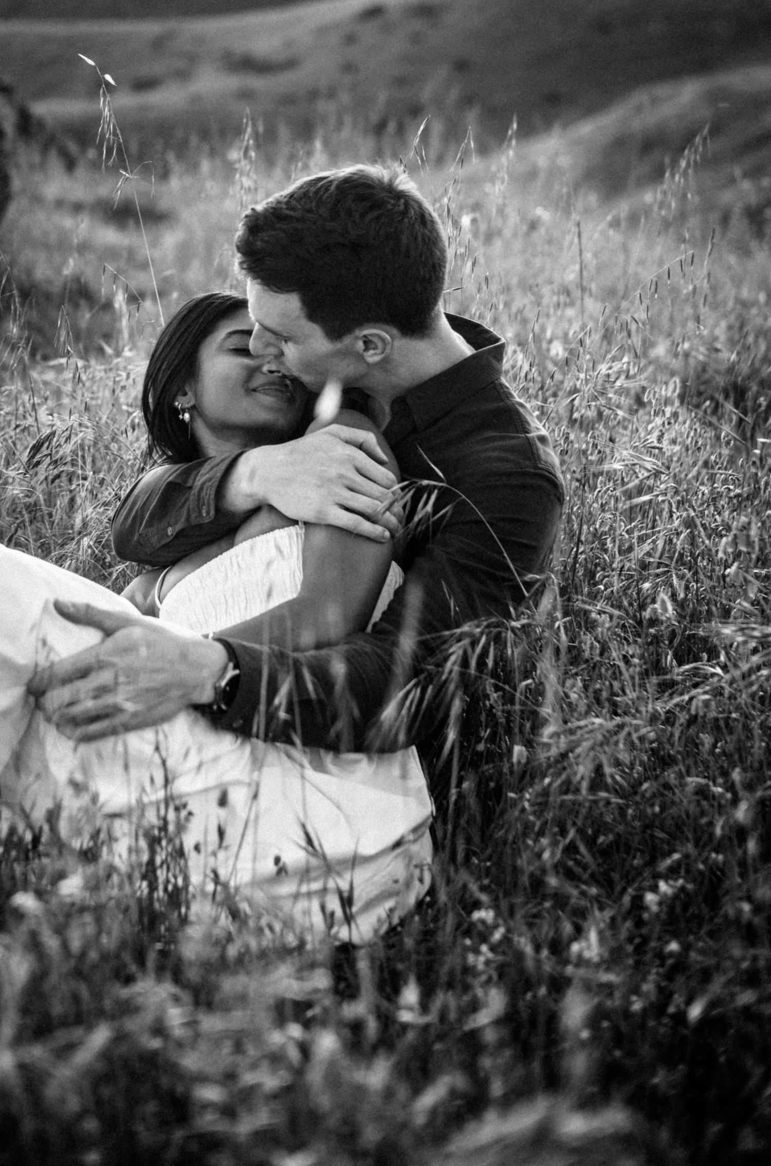 Black and white photo of couple kissing romantically in tall grass field.Photography by The Y.K. Studio.