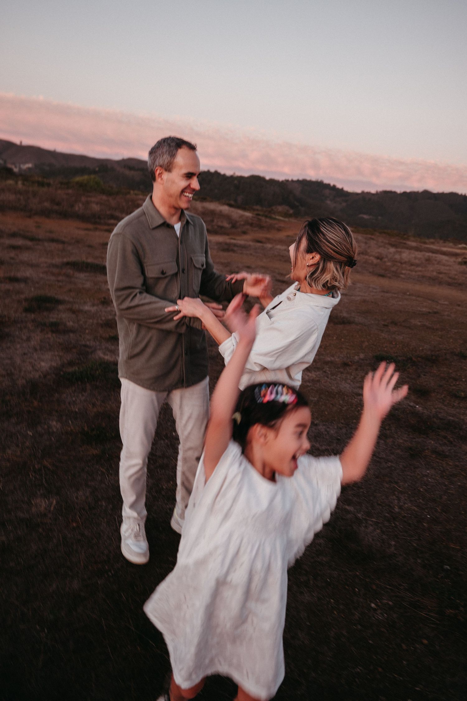 Family enjoying a playful moment together in an open field at dusk.