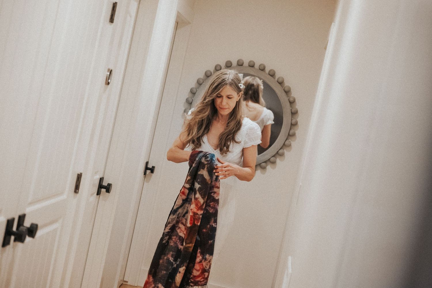 Young woman in white top and floral skirt checking her outfit in a round mirror.