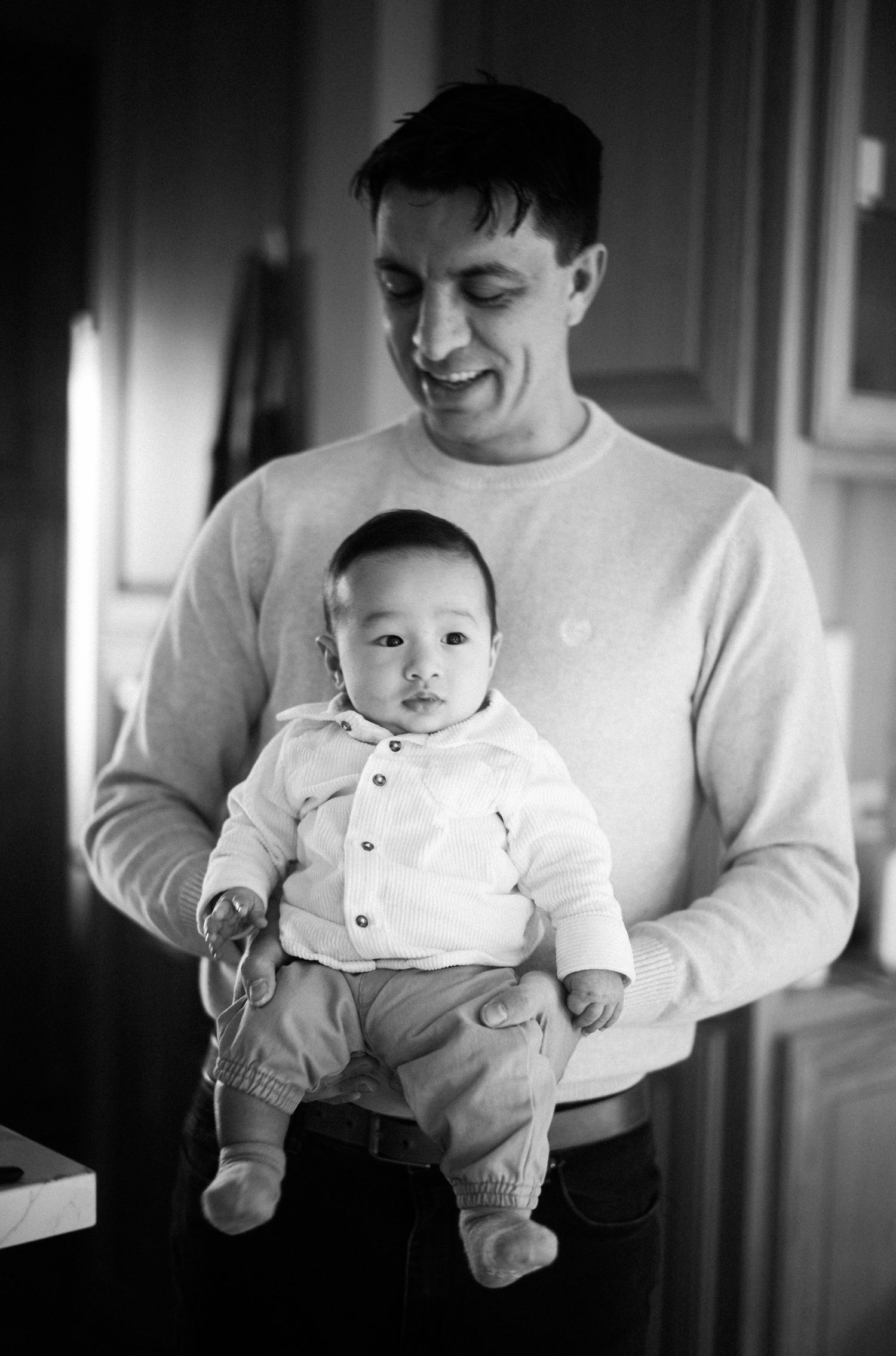Smiling father holding infant baby in black and white indoor portrait photo.