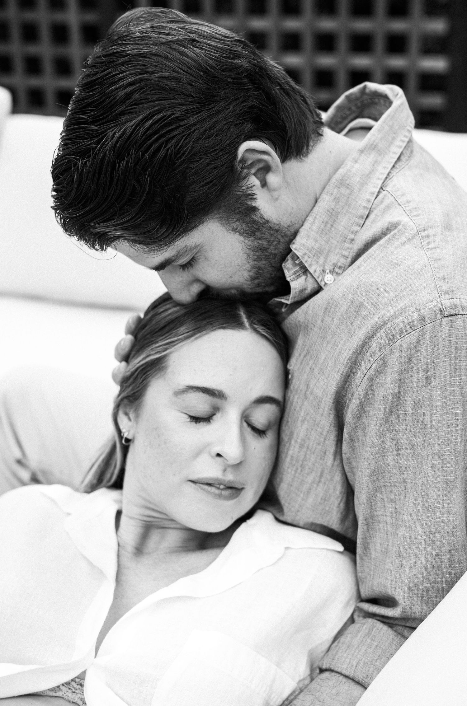 Black and white photo of a couple sharing a tender moment, man kissing woman's head as she rests eyes closed.