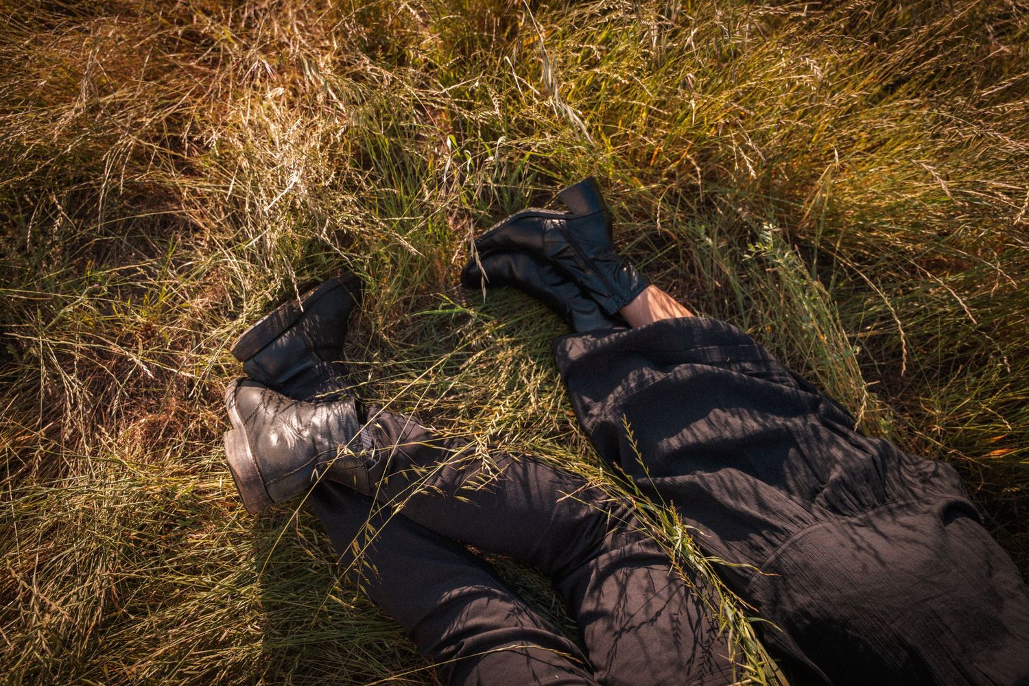 Two people lying in dry golden grass wearing black clothing and boots.Photography by The Y.K. Studio.