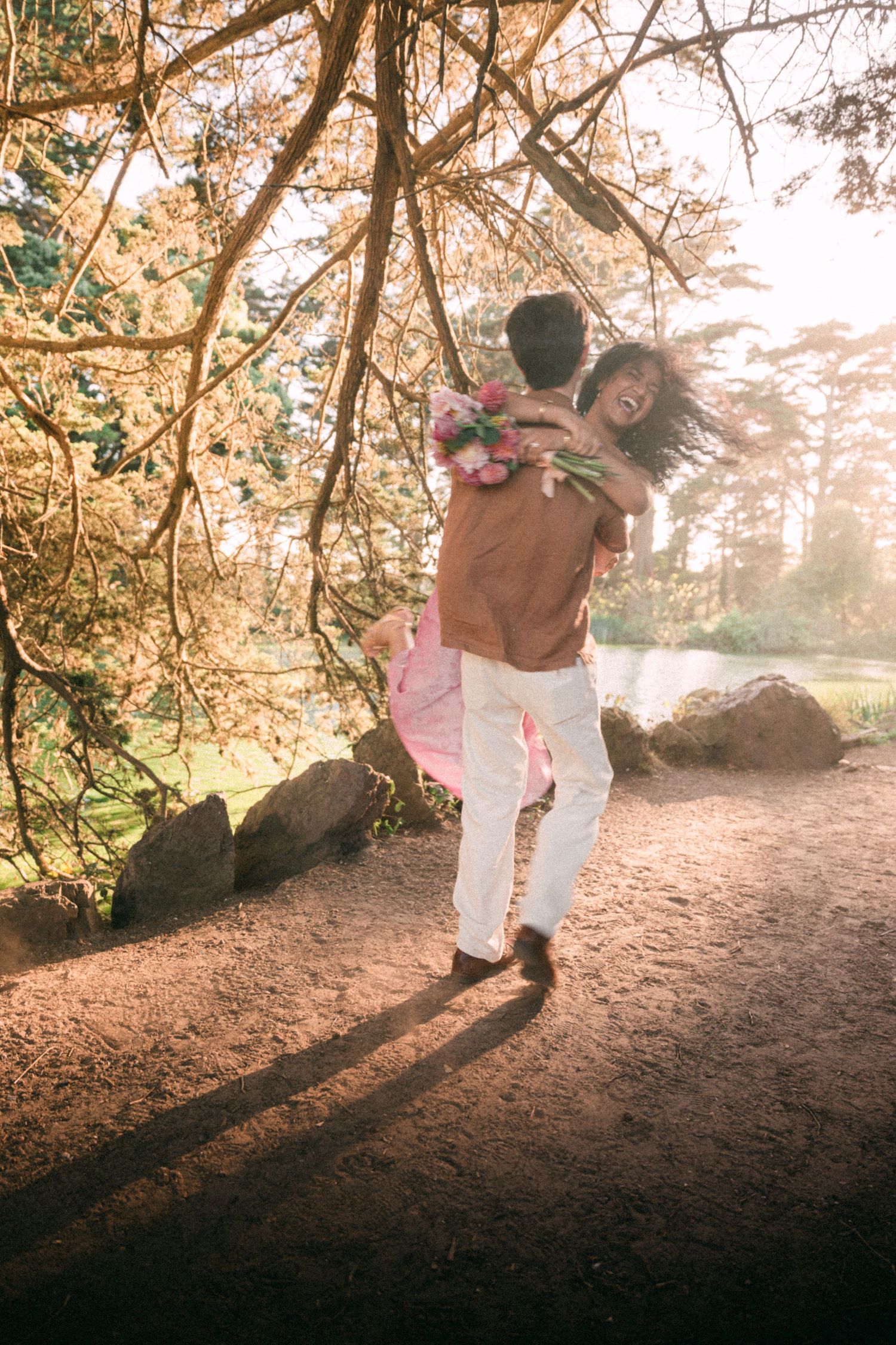 Man lifting and spinning woman in his arms under golden trees in a sunlit park.
