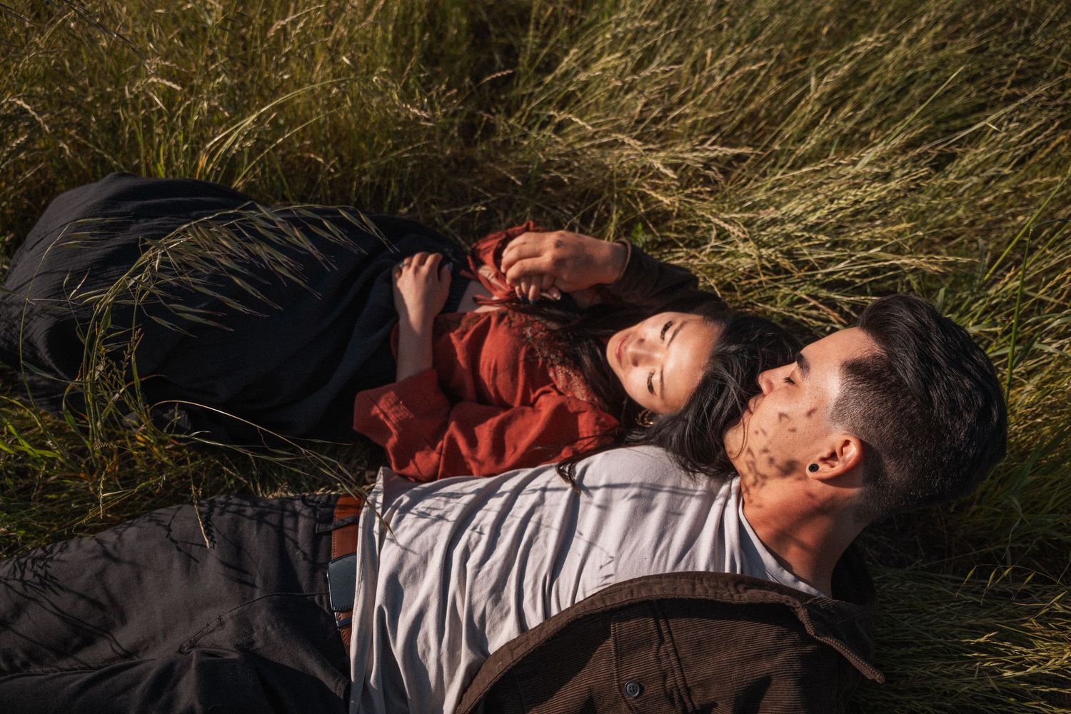 Couple lying together in tall green grass, smiling and relaxed in warm golden sunlight.Photography by The Y.K. Studio.