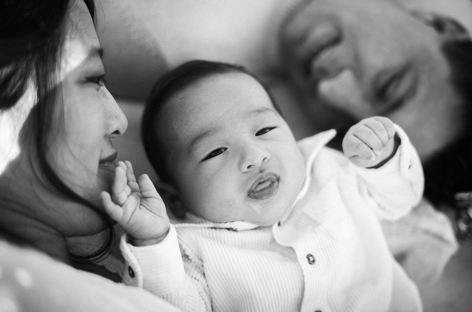 Newborn baby making funny face between two parents in tender black and white close-up.