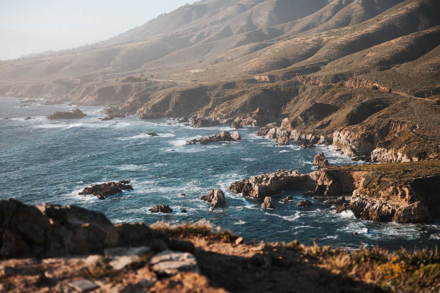 Rocky California coastline with crashing waves and misty hills along Big Sur.