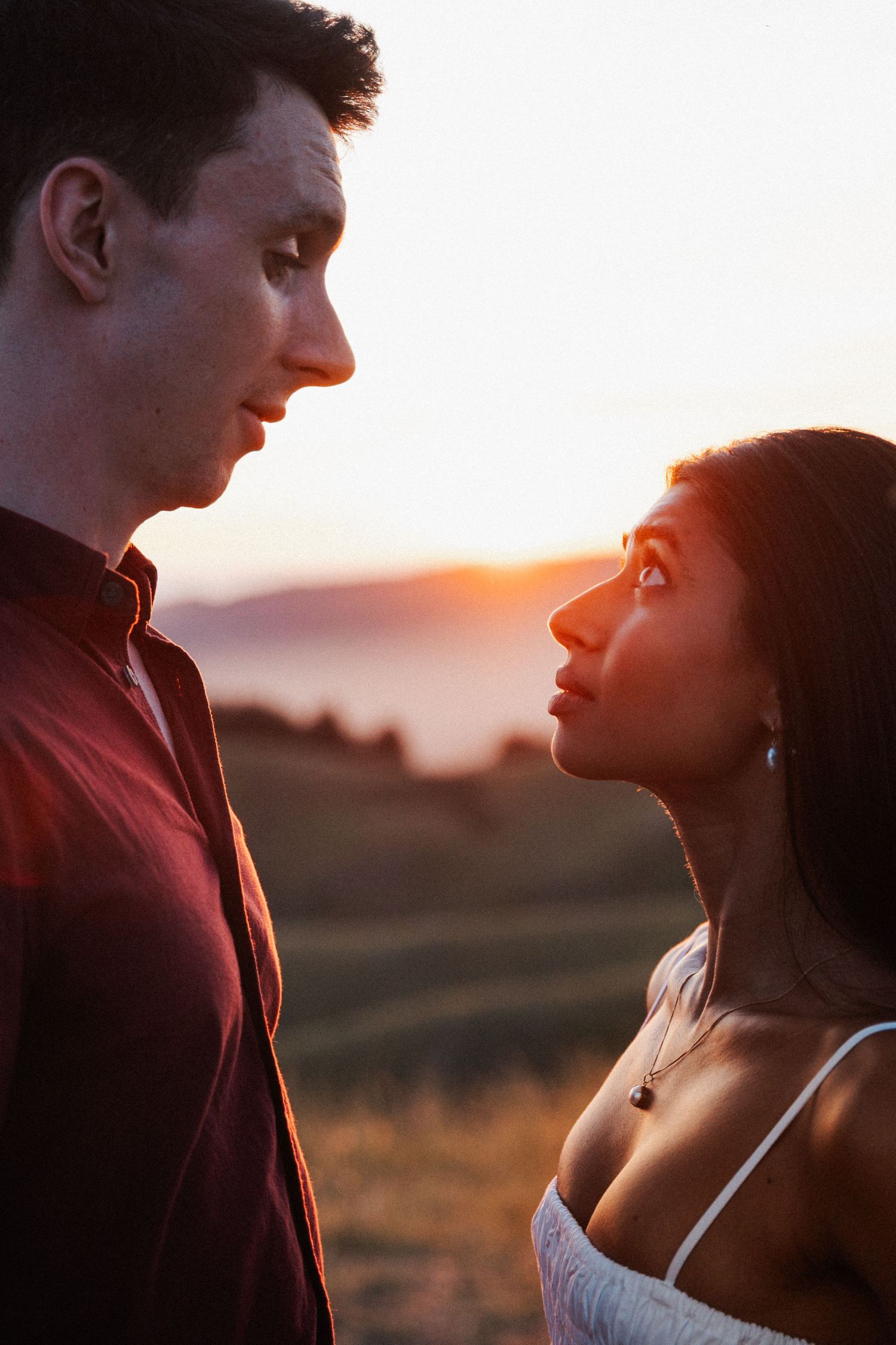 Intimate close-up portrait of interracial couple facing each other with warm golden sunset glow behind them.