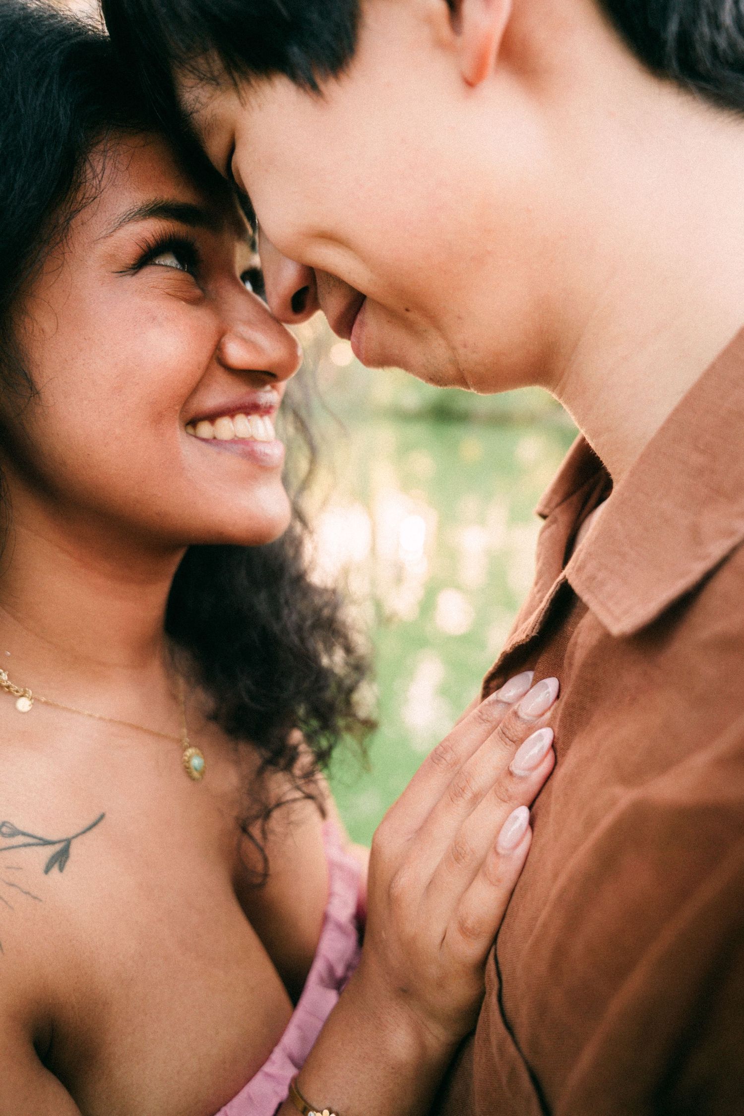 A joyful interracial couple sharing an intimate moment, smiling face-to-face outdoors in warm natural light.