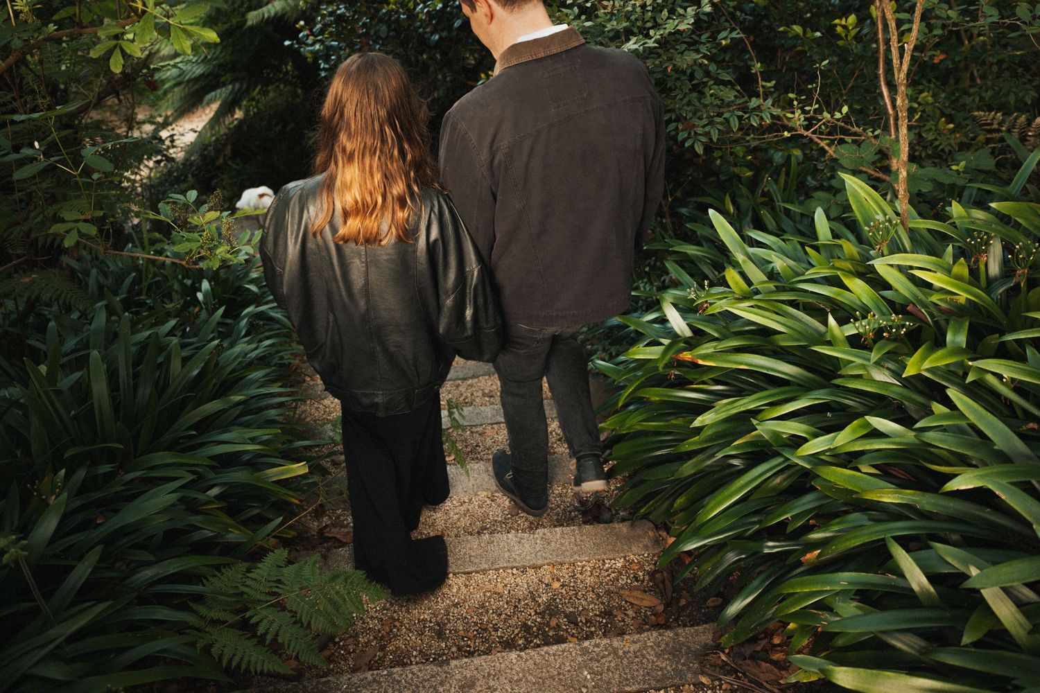 Two people walking up stone garden steps surrounded by lush green tropical plants and foliage.