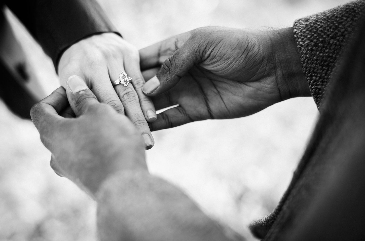 Black and white photo of a couple exchanging rings during a wedding ceremony, close-up of hands.