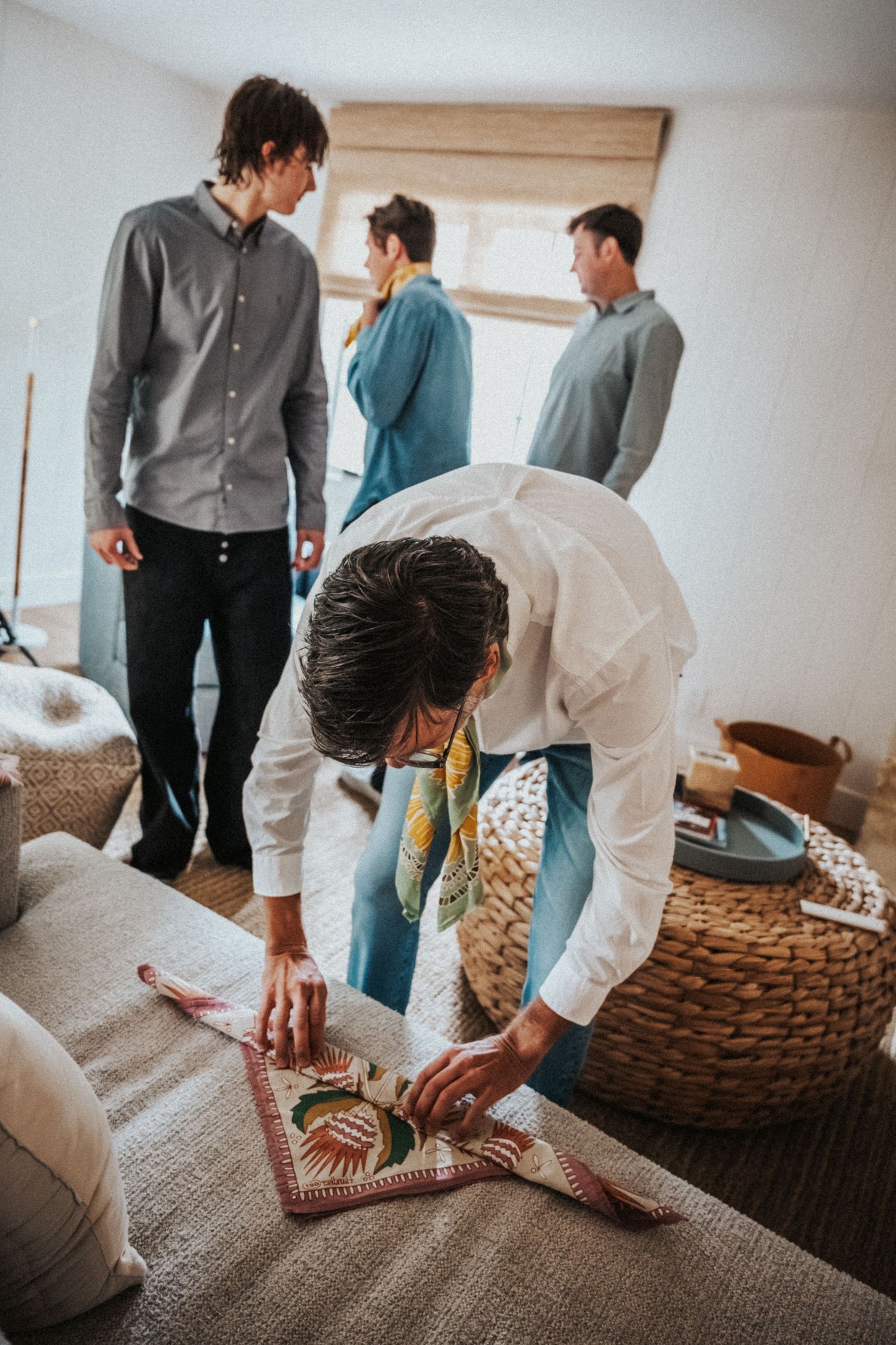 People gathering in a cozy room, one person arranging a decorative rug on a sofa while others stand nearby.