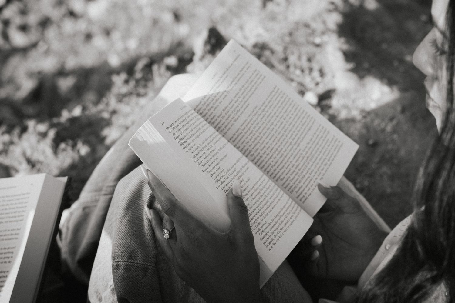 Person reading an open book outdoors in black and white photo.