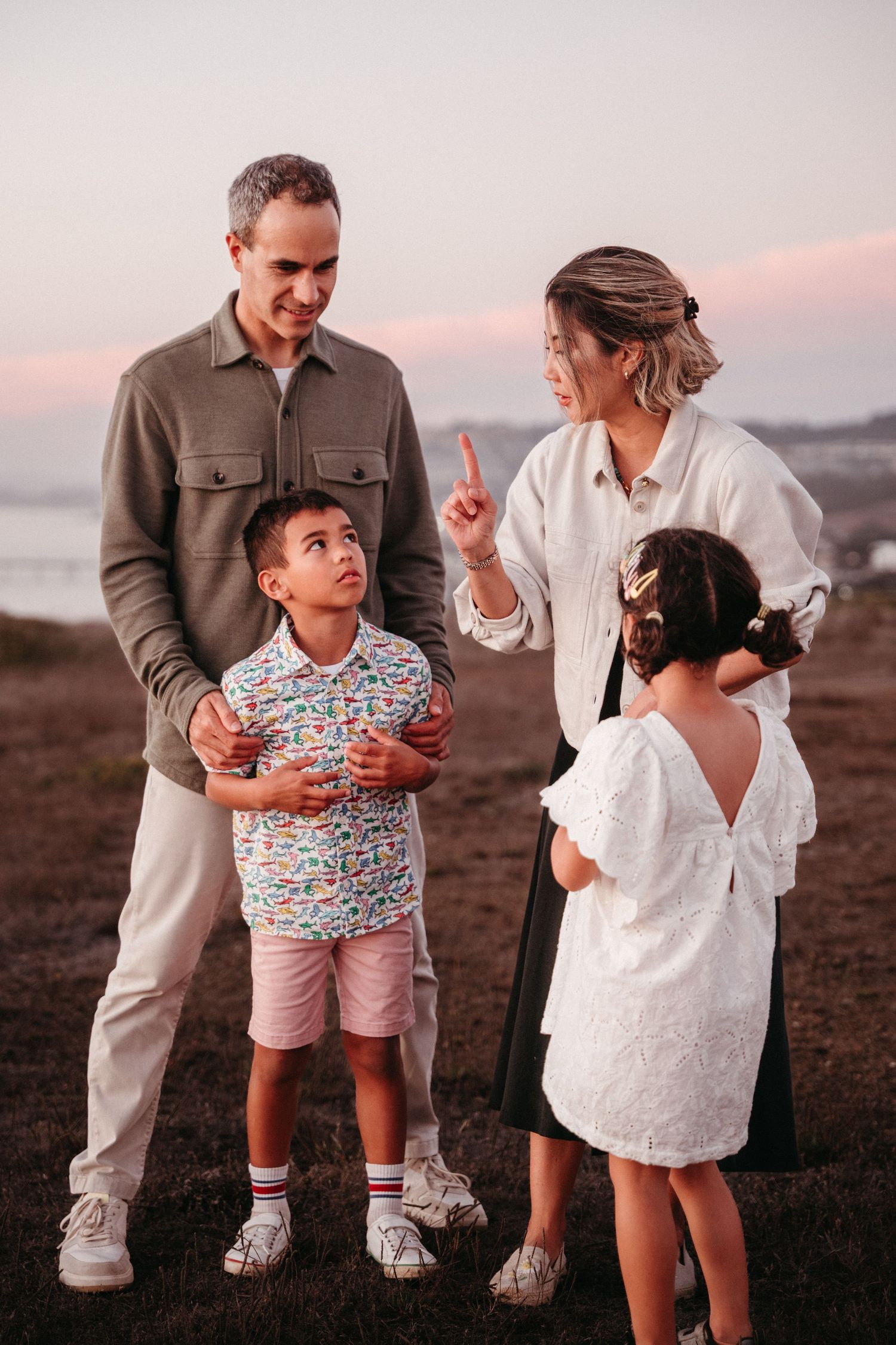 Family of four sharing a moment outdoors at sunset near the coast.