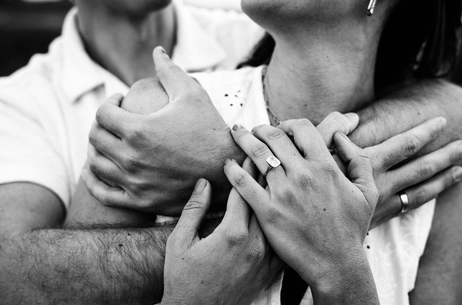 Black and white photo of a couple embracing, hands intertwined showing an engagement ring.Photography by The Y.K. Studio.