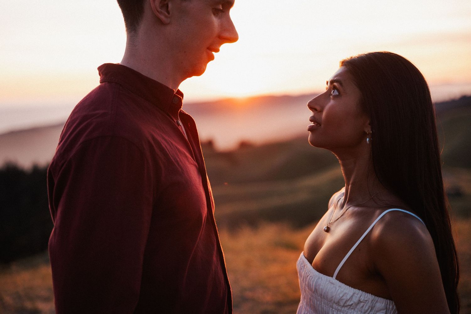 A couple shares a romantic moment at sunset on a hilltop, with the woman gazing up at the man in golden light.Photography by The Y.K. Studio