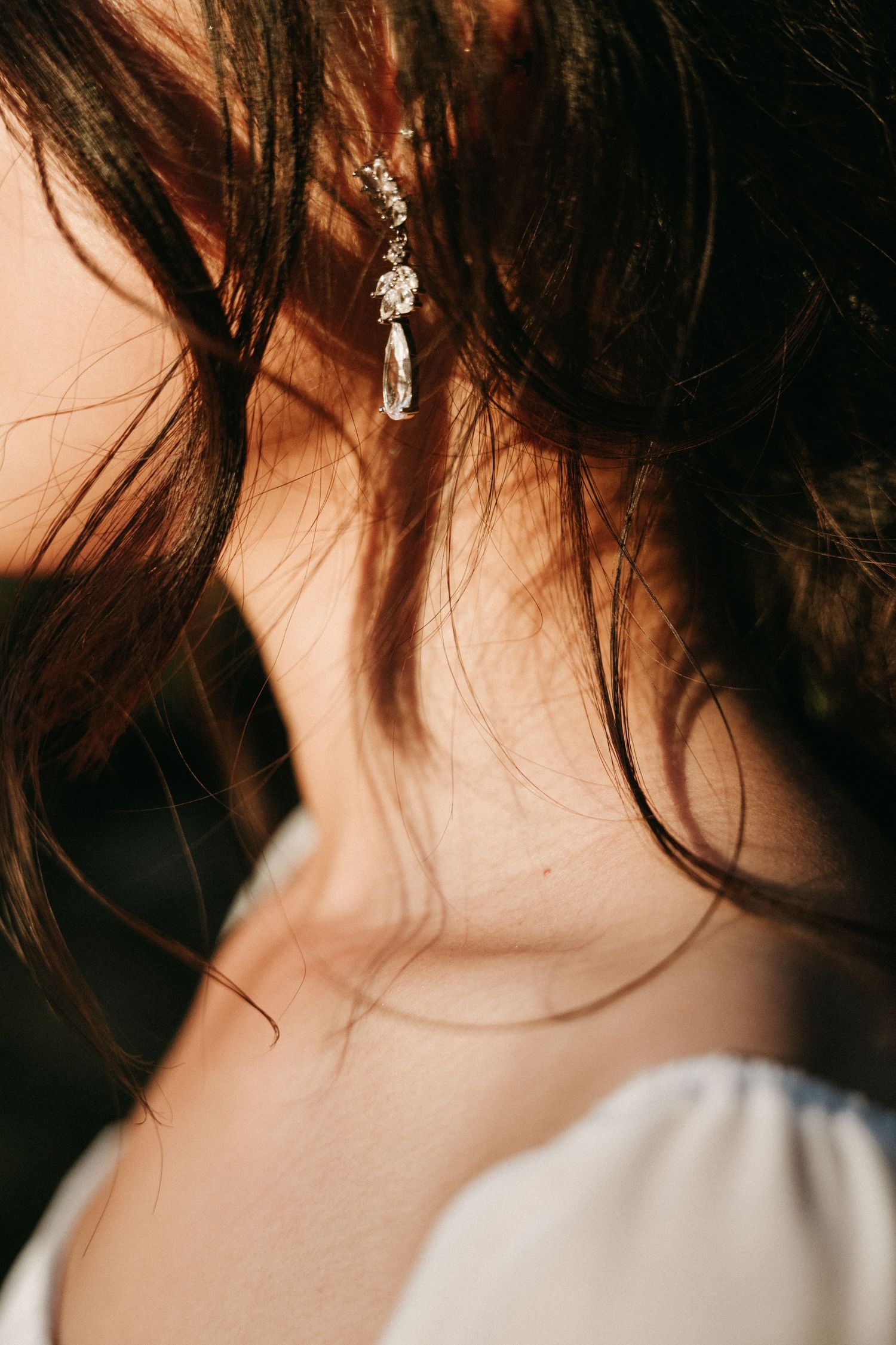 Close-up of a bride wearing an elegant crystal drop earring with soft sunlight on her dark hair.