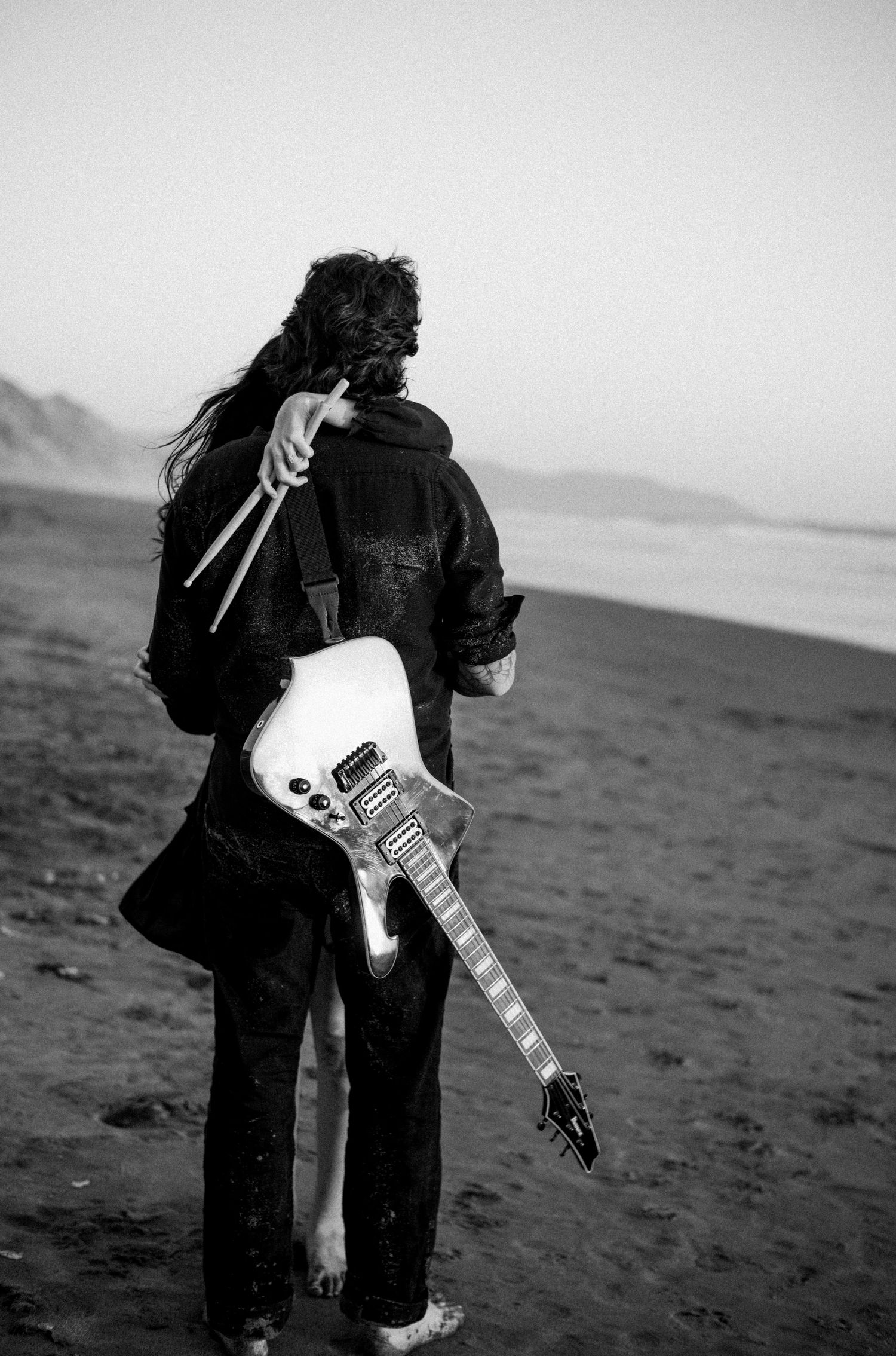 Person holding white electric guitar on beach in black and white photo.Photography by The Y.K. Studio.