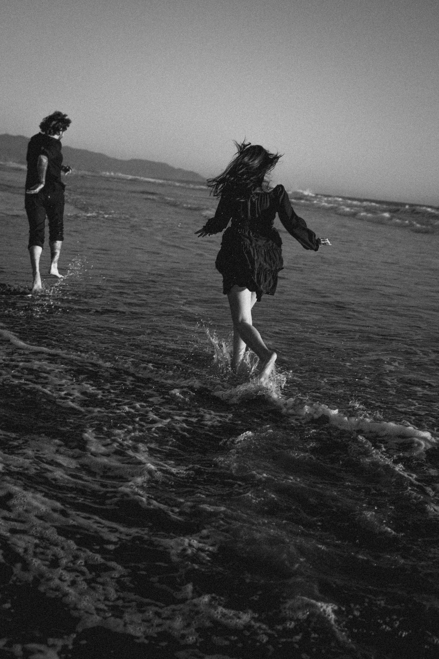 Couple playing in ocean waves on beach at dusk in black and white.