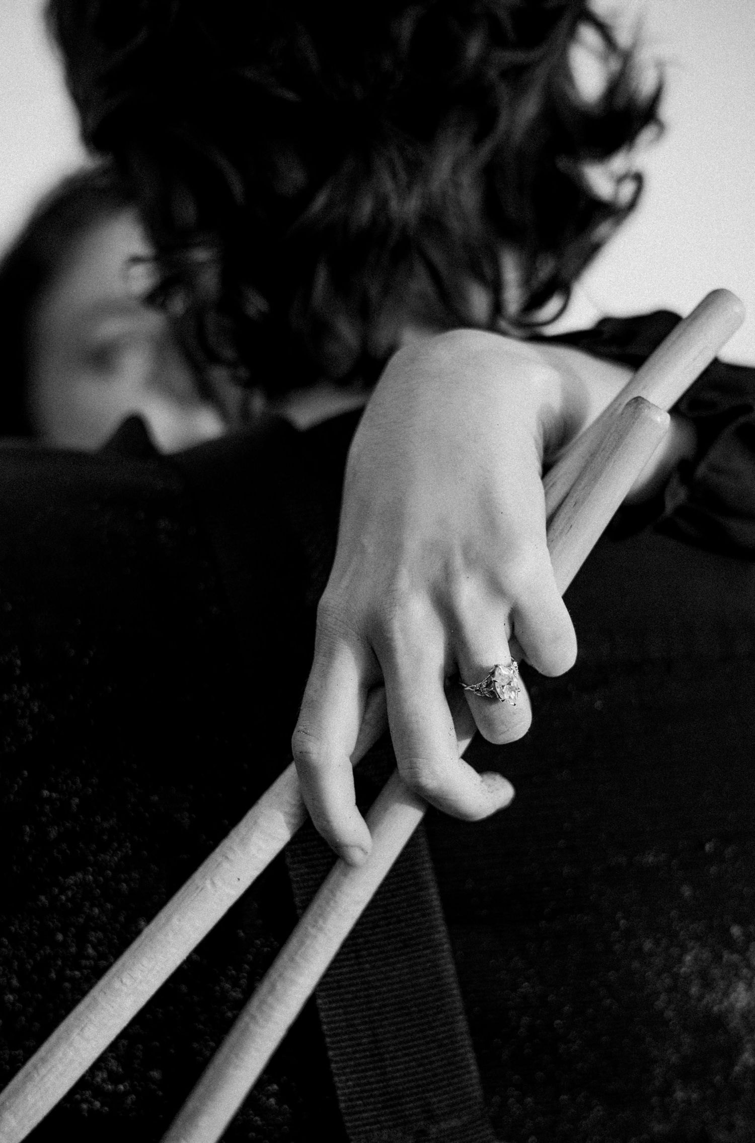 Close-up of a hand holding drumsticks with a decorative ring in black and white photography.