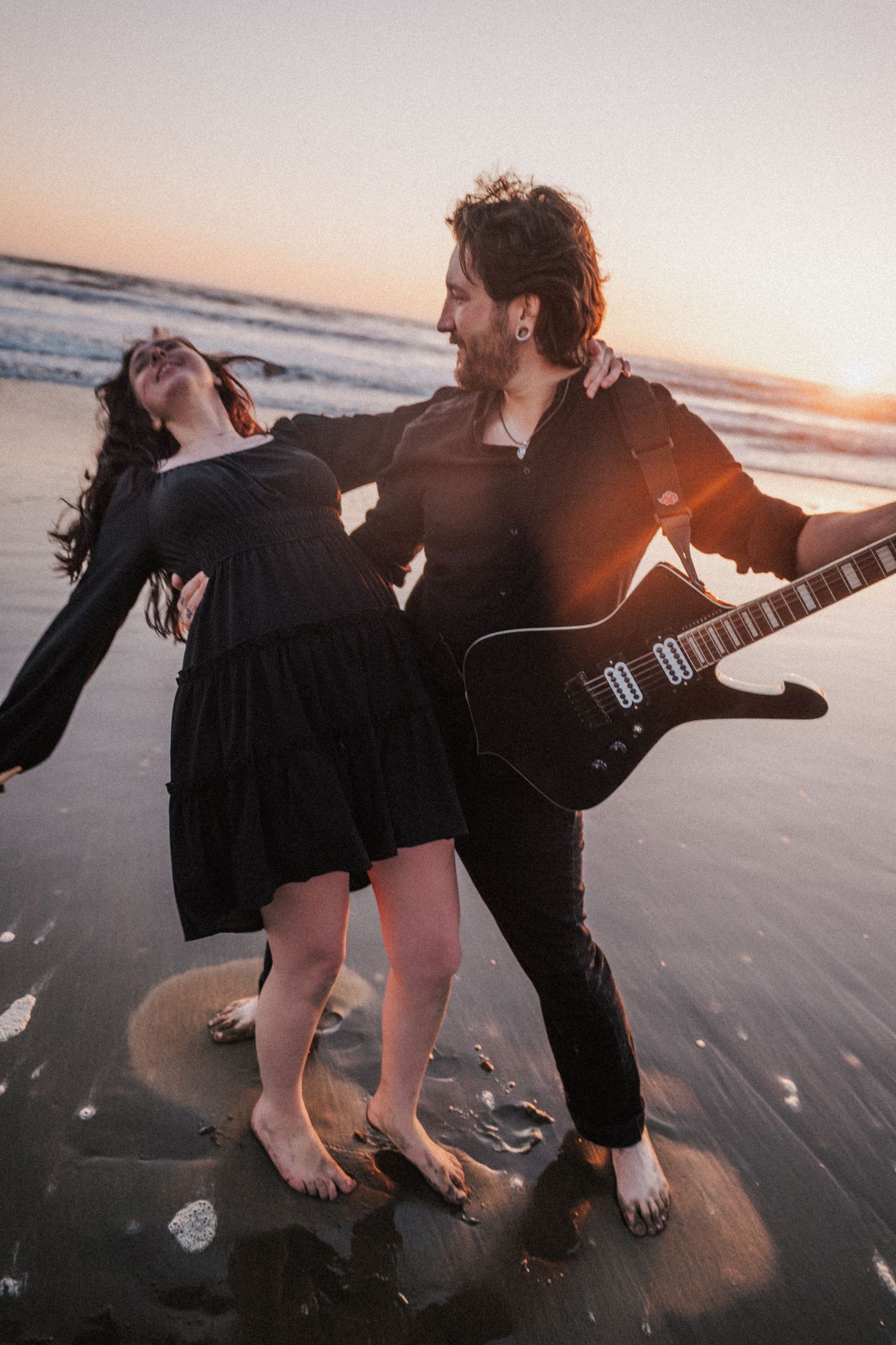 Couple dancing barefoot on beach at sunset, man holding black electric guitar.