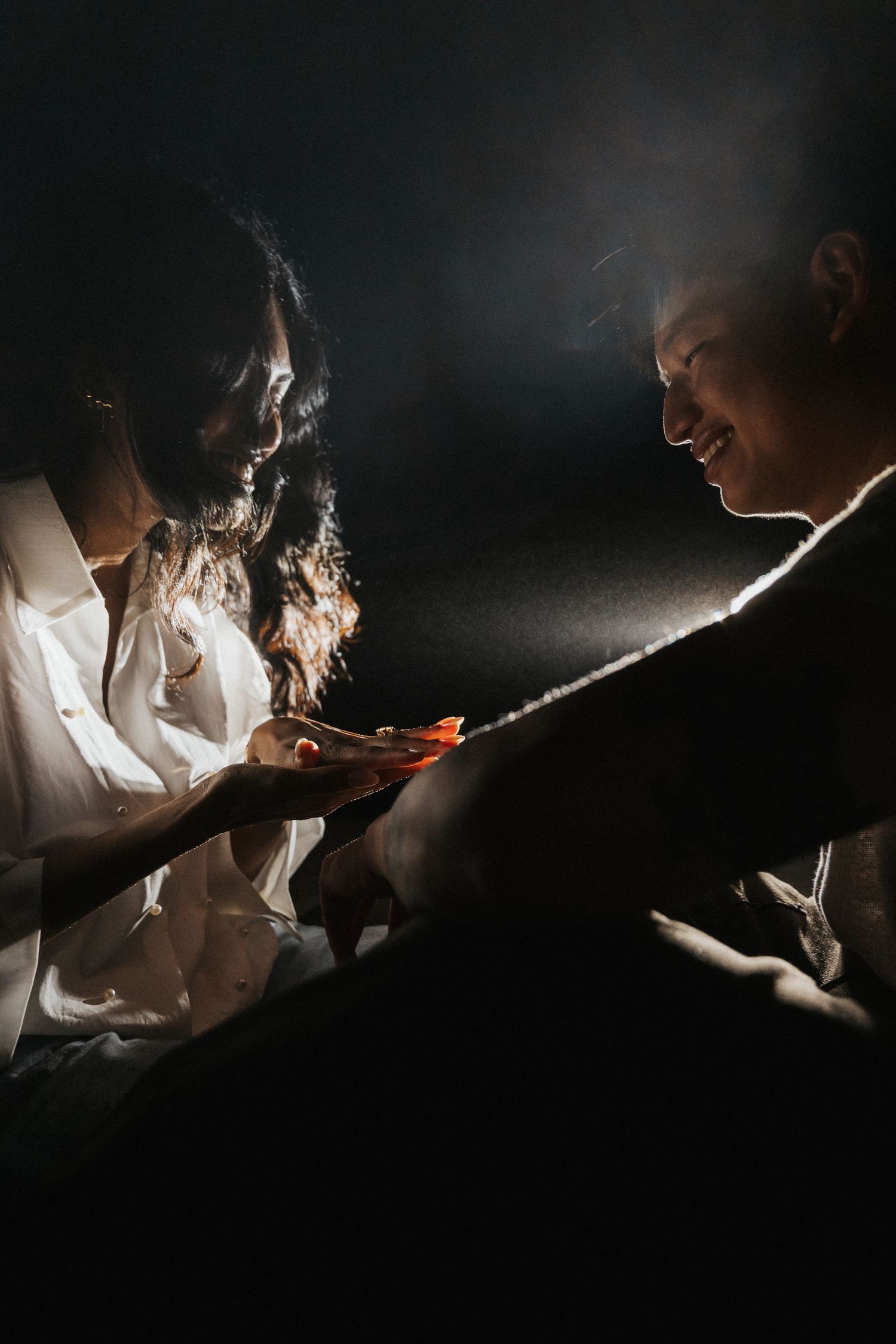 Two people sharing a candlelit moment in darkness, illuminated by warm glowing light in an intimate setting.