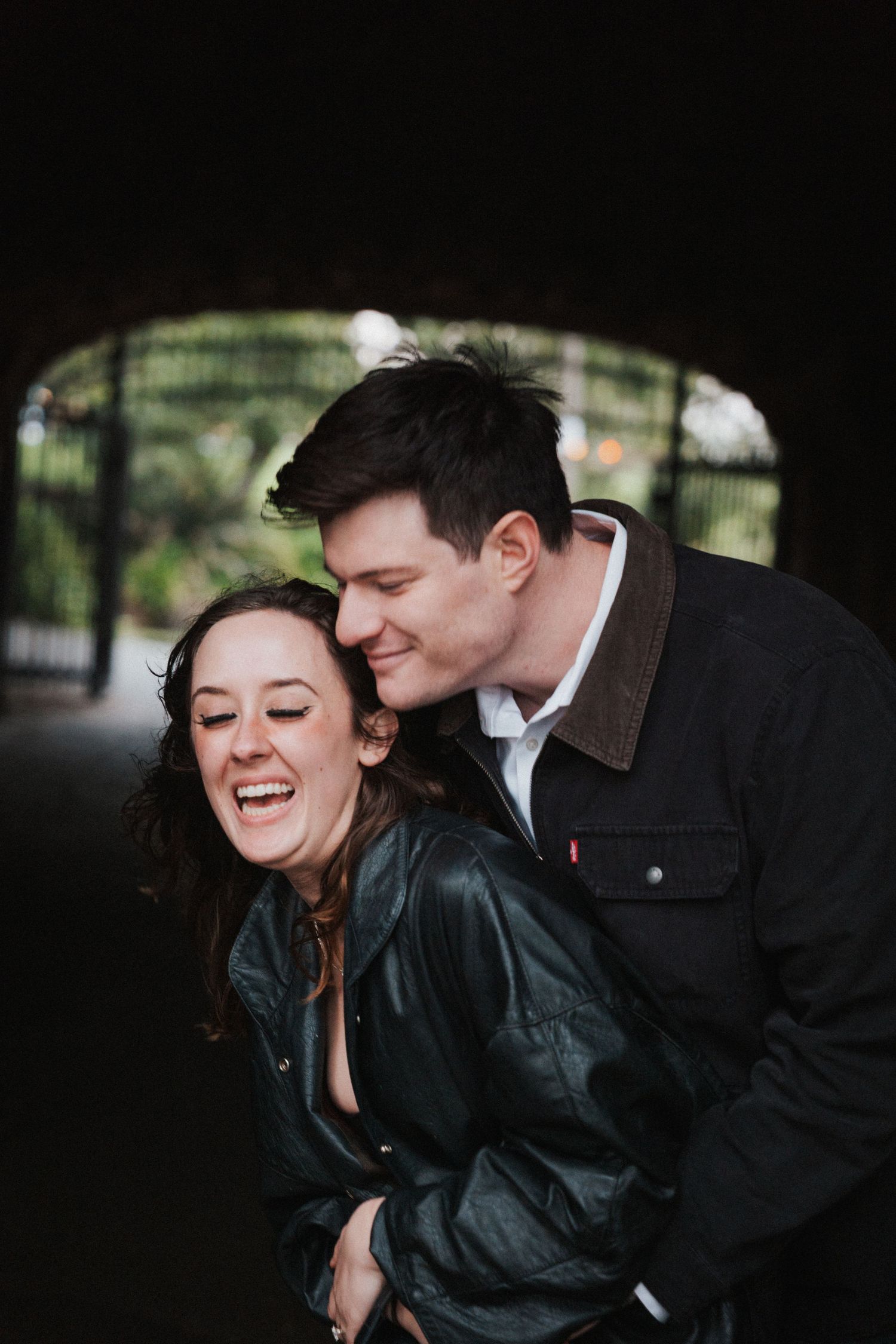 Happy couple sharing a playful moment under a dark archway, woman laughing as man hugs her from behind.