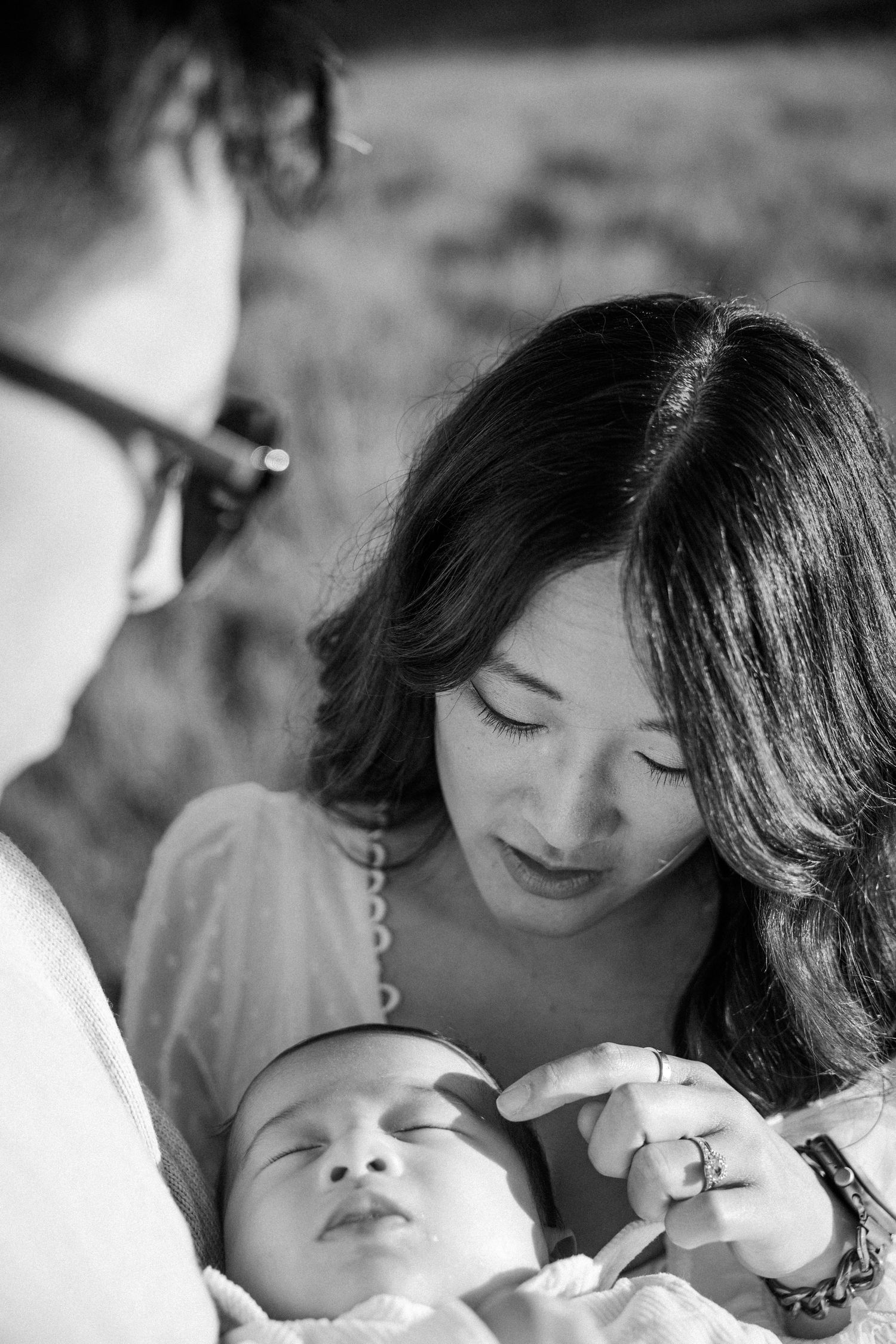 Black and white close-up of mother tenderly touching sleeping newborns face with father nearby.