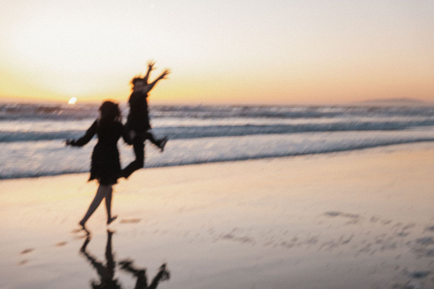 Two people joyfully running on a beach at sunset, with ocean waves and warm golden sky in the background.