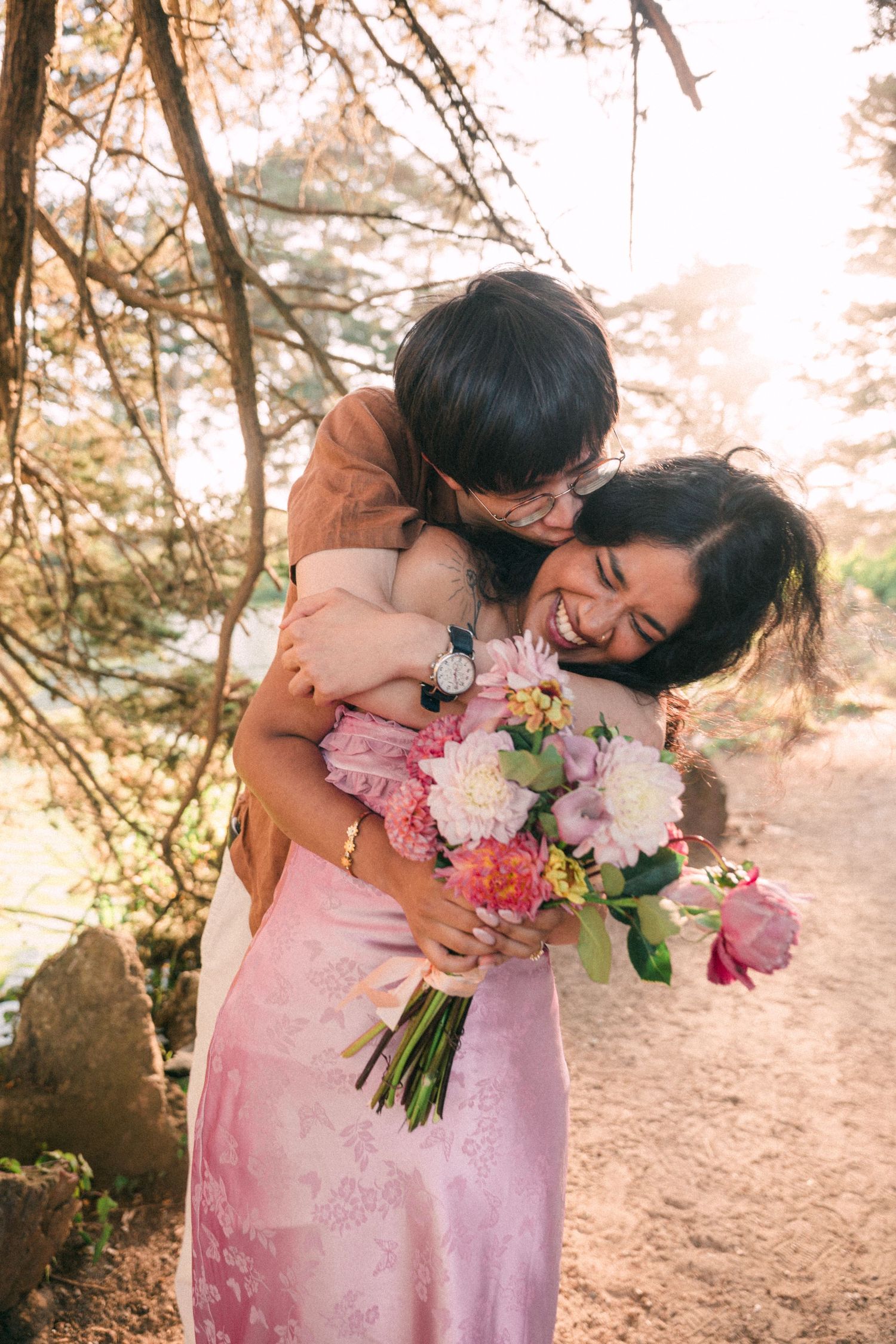 Joyful couple embracing after engagement, woman holding a colorful bouquet of pink and white flowers.