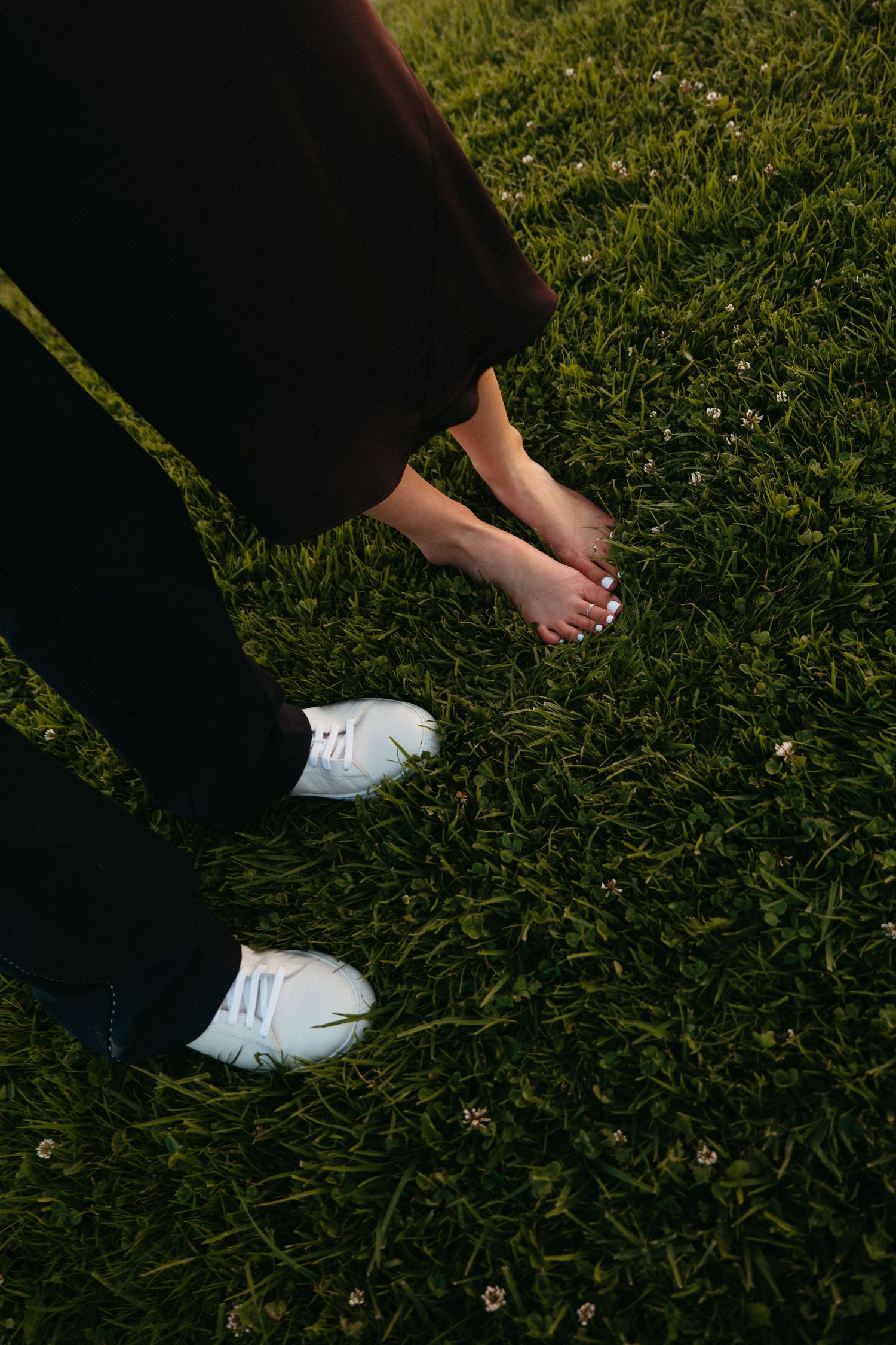 Two people stand on lush green grass, one barefoot and one wearing white sneakers, captured from below.